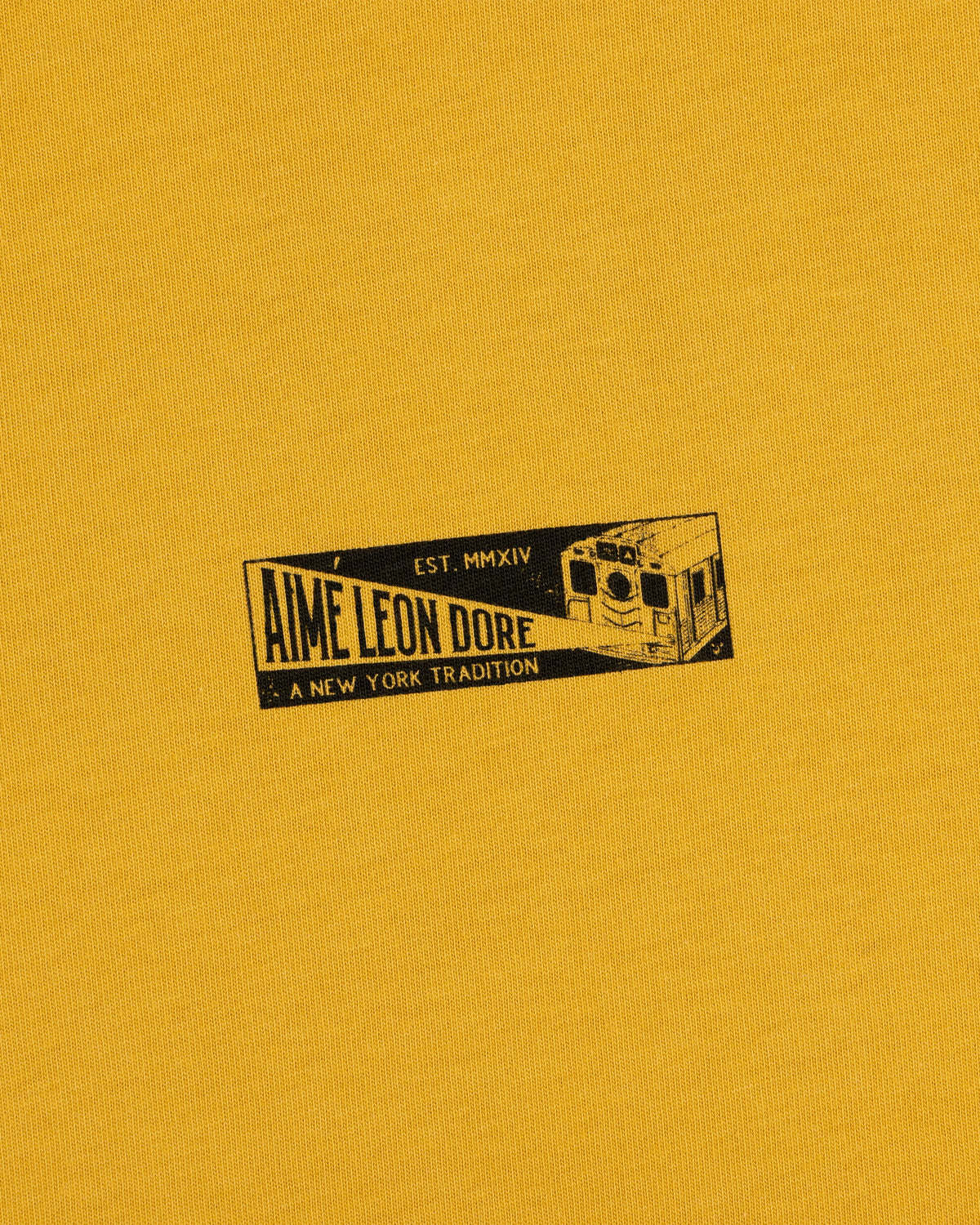 Mustard yellow Aimé Leon Dore Transit Tee with subway car graphic, text: Aime Leon Dore, Est. MMXIV, A New York Tradition.
