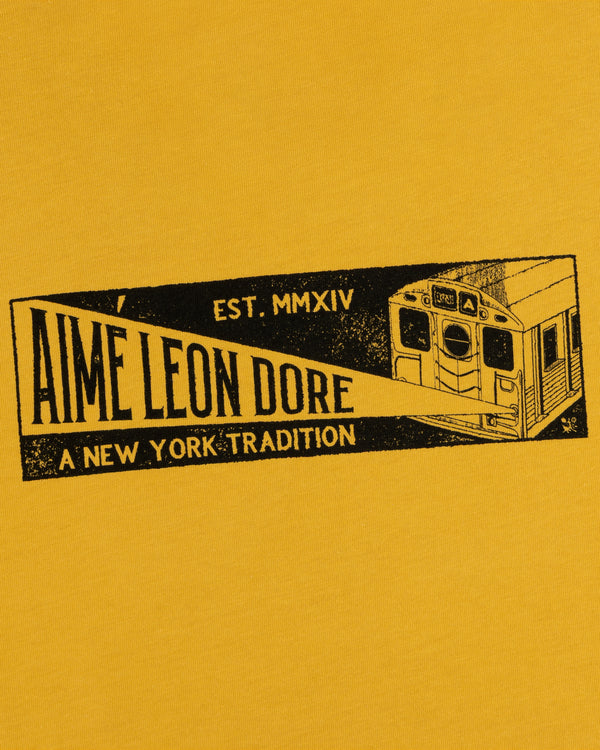 Mustard yellow Aimé Transit Tee featuring a graphic of a subway car and the text Aime Leon Dore, A New York Tradition.