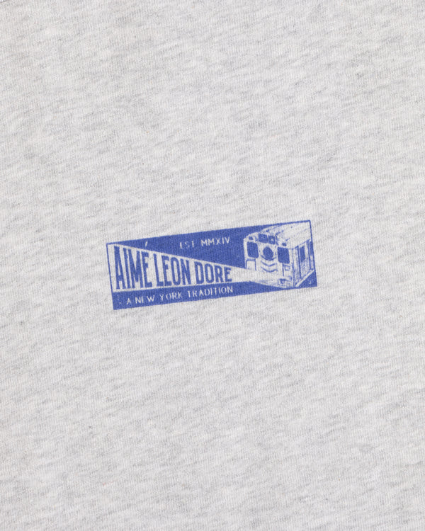 Gray heathered Aimé Transit Tee with a blue graphic of a subway car and text reading Aime Leon Dore A New York Tradition.