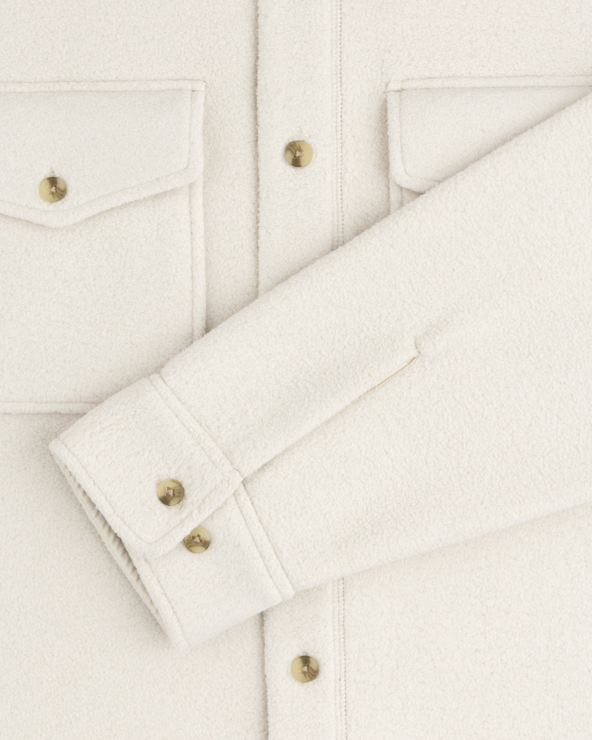 Close-up of the Melange Fleece Shirt in off-white with gold buttons, flap pockets, and a folded sleeve across the front.