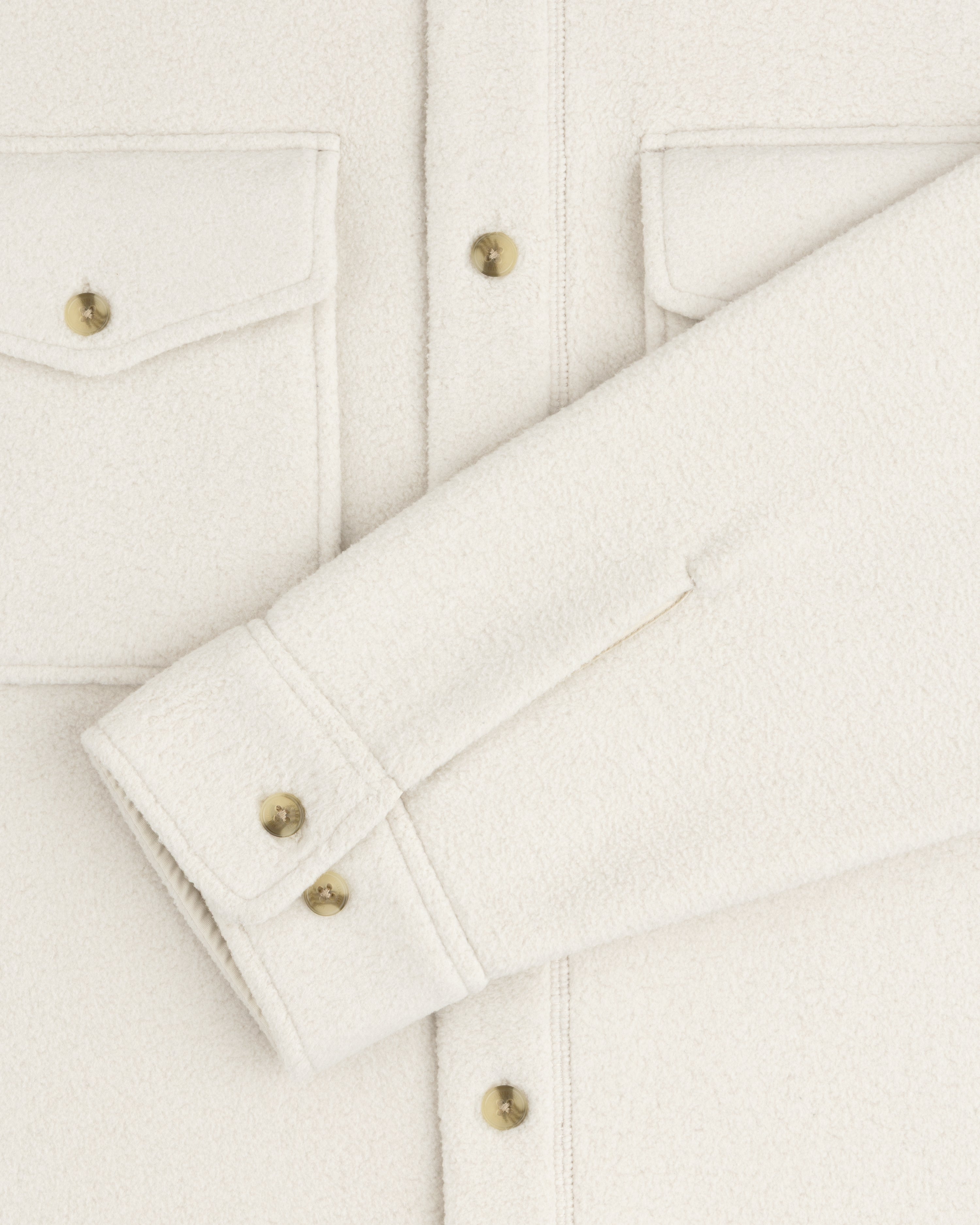 Close-up of the Melange Fleece Shirt in off-white with gold buttons, flap pockets, and a folded sleeve across the front.