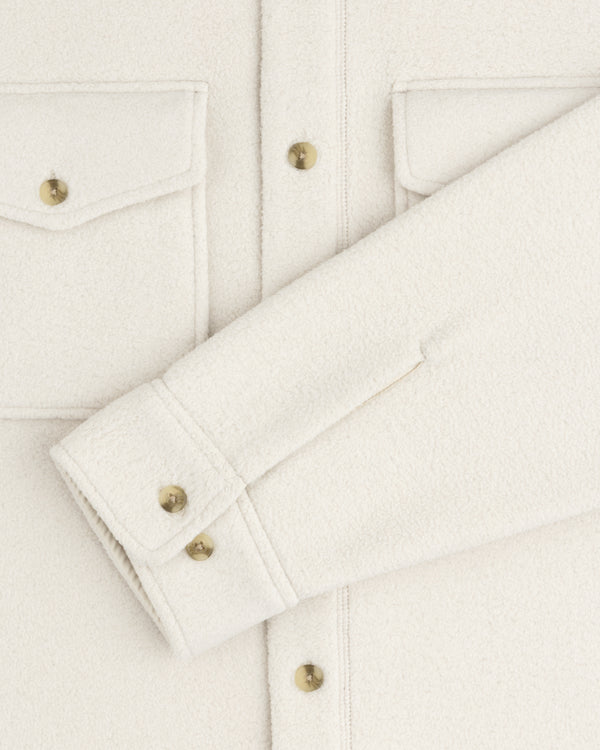 Close-up of the Melange Fleece Shirt in off-white with gold buttons, flap pockets, and a folded sleeve across the front.