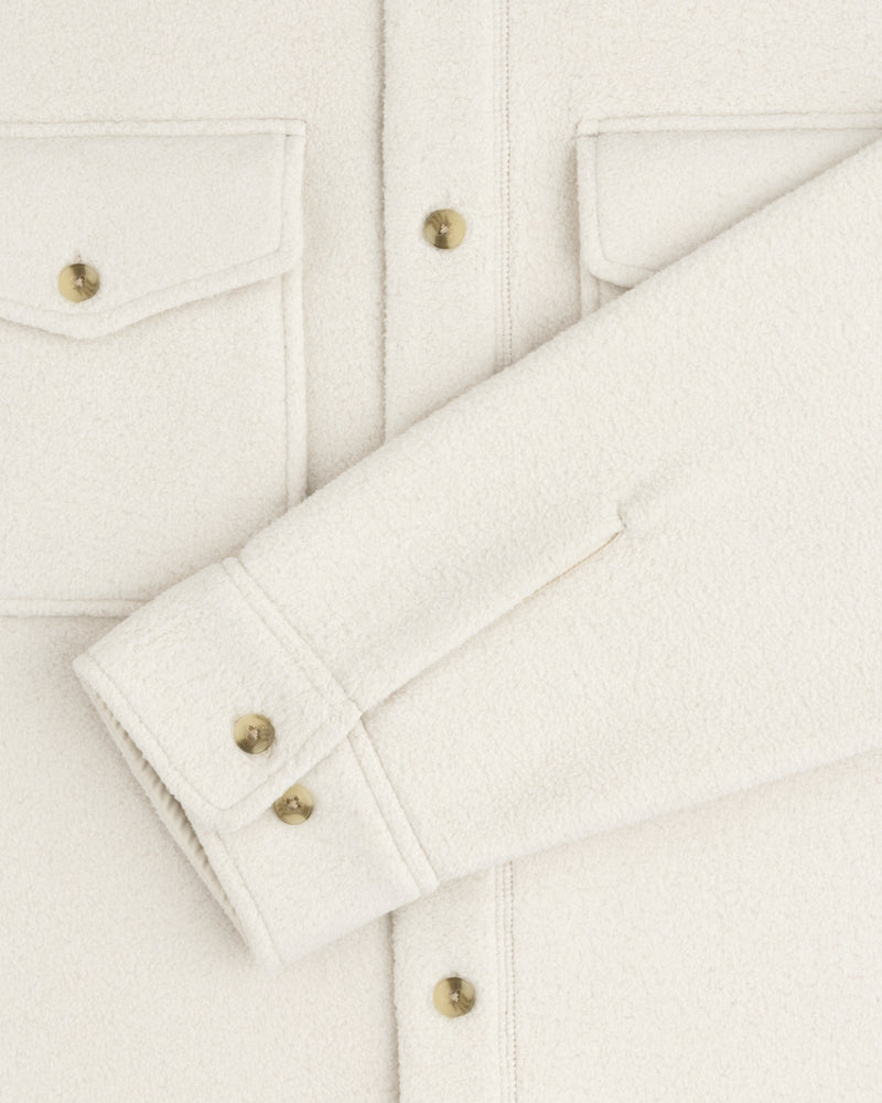 Close-up of the Melange Fleece Shirt in off-white with gold buttons, flap pockets, and a folded sleeve across the front.