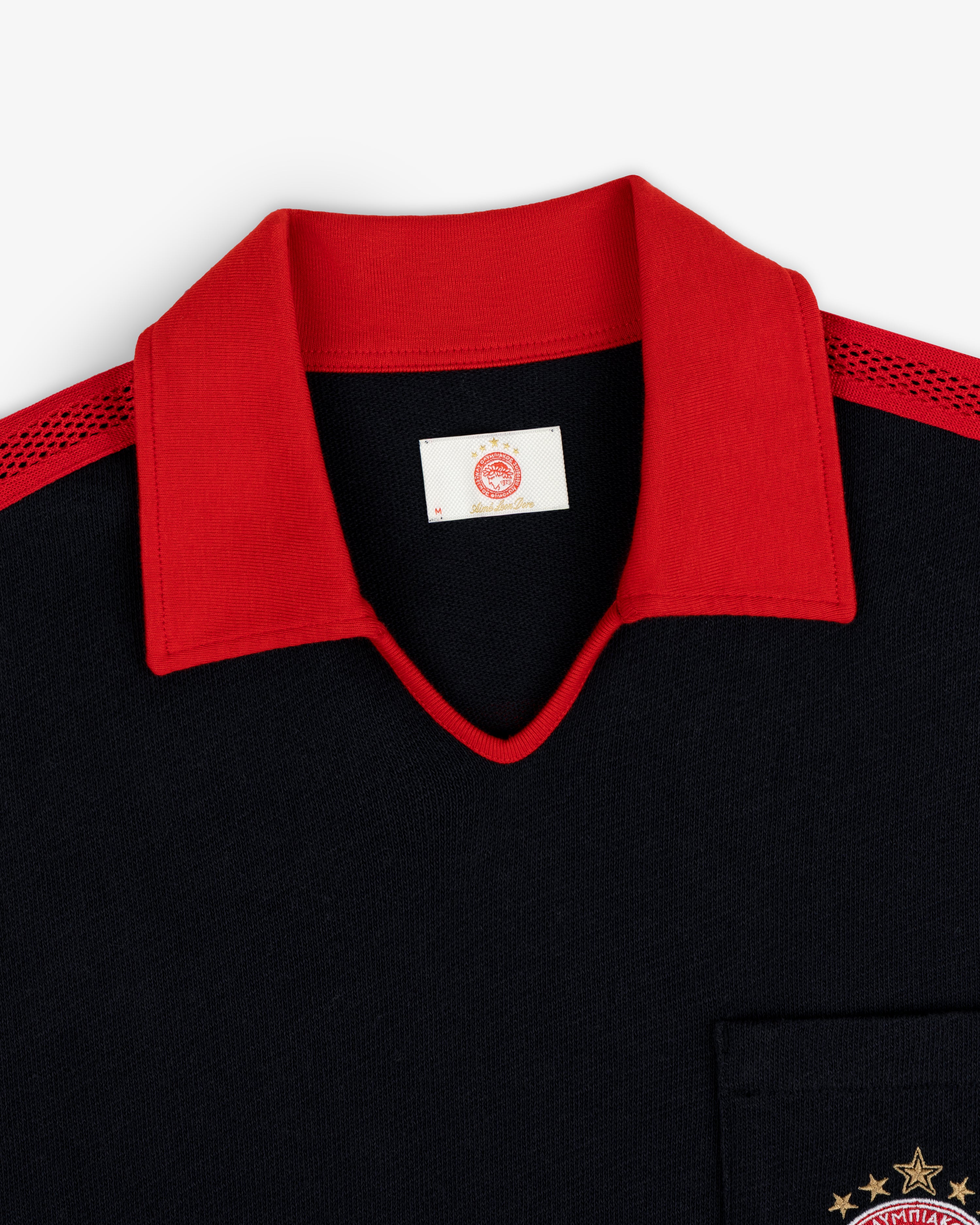 ALD / Olympiacos F.C. Heritage Ringer Polo: black shirt with a red collar, red mesh shoulders, and a gold embroidered emblem.