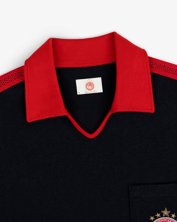ALD / Olympiacos F.C. Heritage Ringer Polo: black shirt with a red collar, red mesh shoulders, and a gold embroidered emblem.