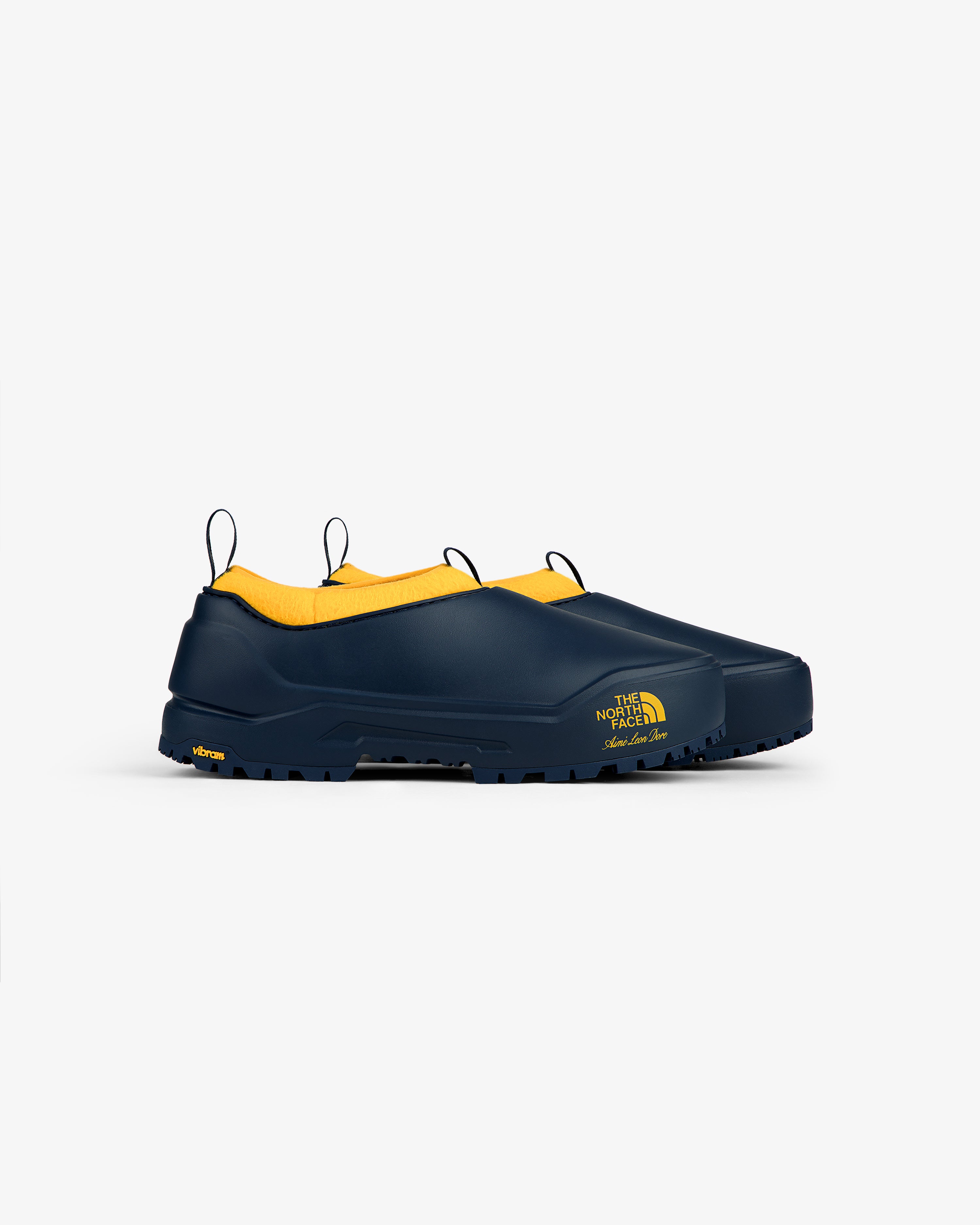 ALD / The North Face Base Camp Mule: Navy slip-ons with yellow interior and logo, on a white background.
