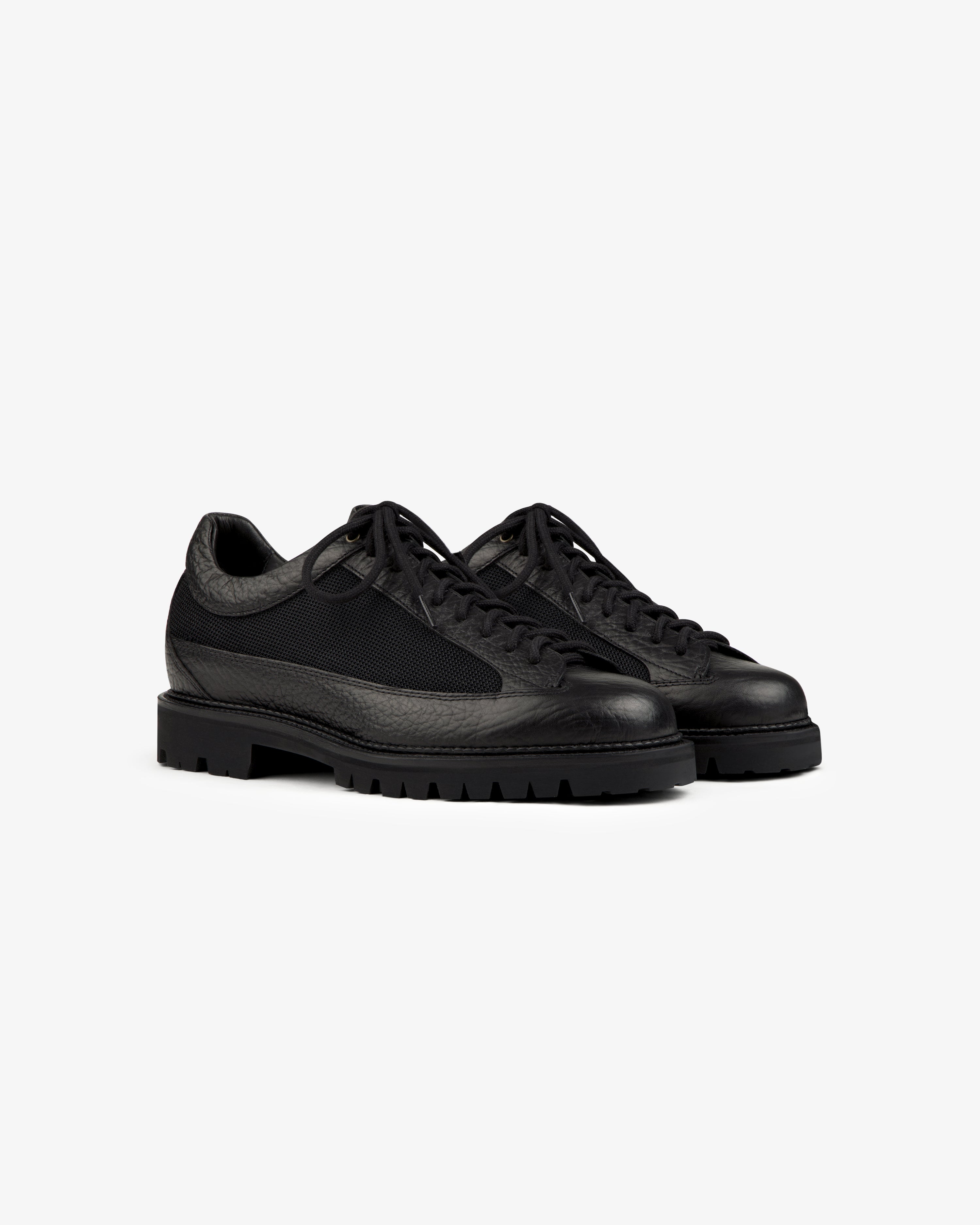 Field Boot black low-top lace-up shoes with textured leather panels, mesh inserts, and lugged rubber soles.