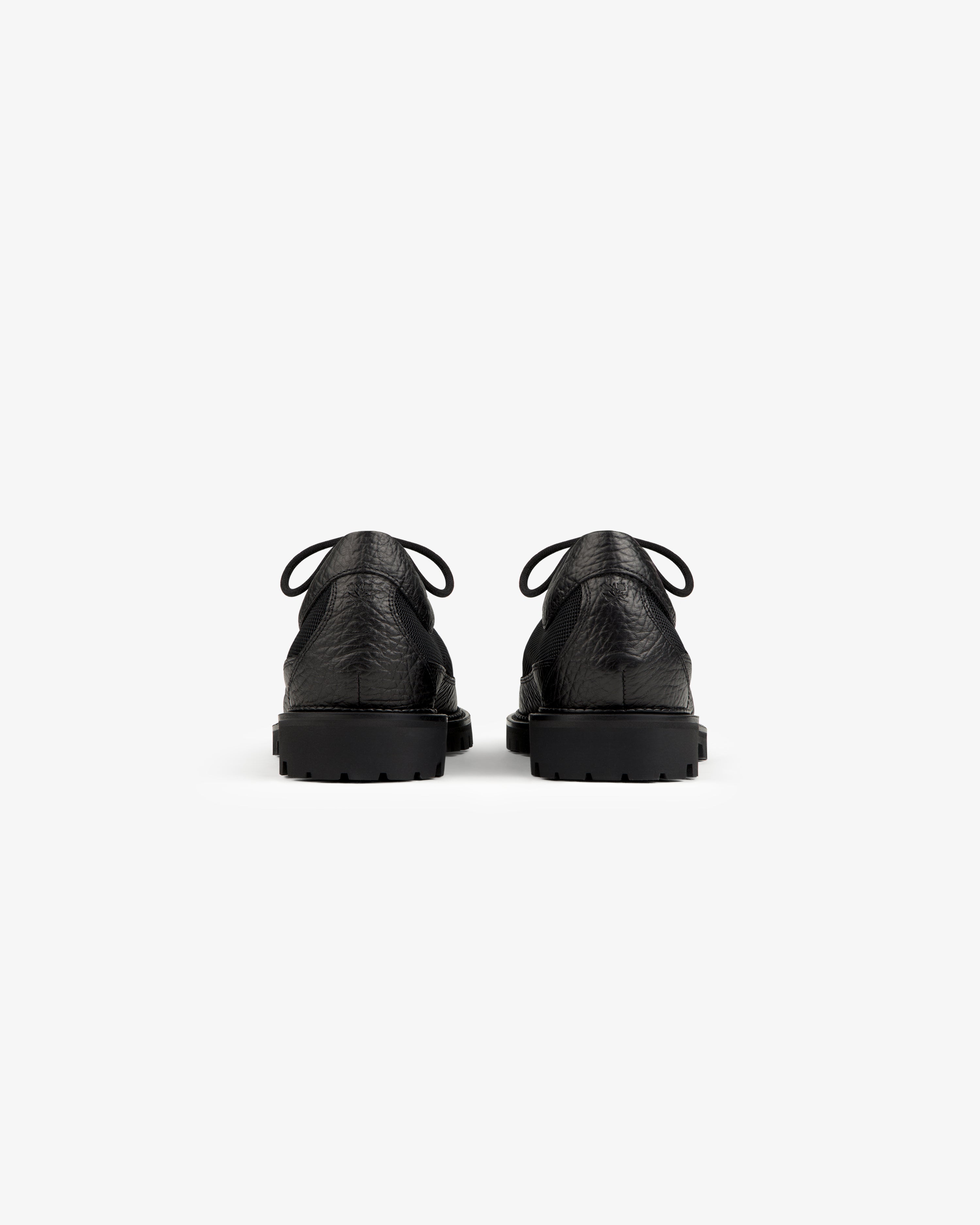 Back view of a pair of black Field Boot lace-up shoes with thick, lugged rubber soles.