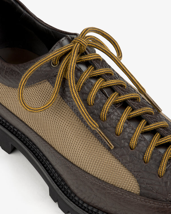 Field Boot in dark brown and tan with a thick lugged sole and yellow-striped laces.
