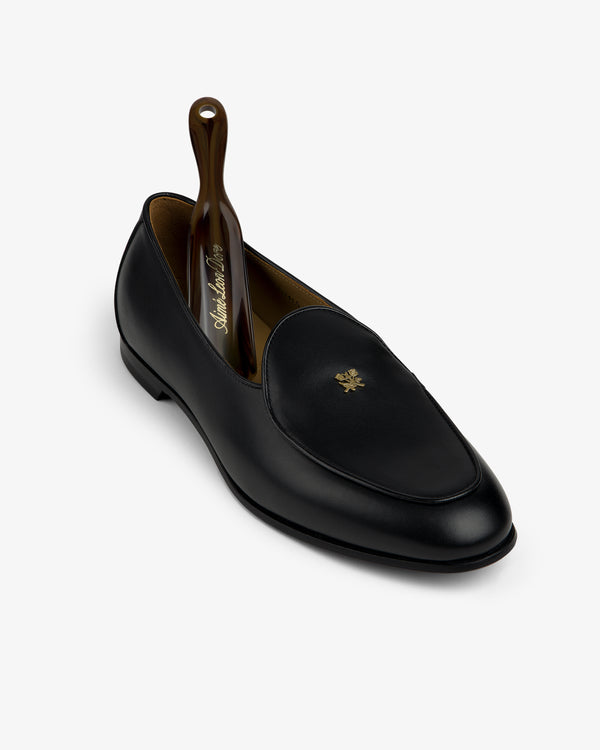 Crest Salóni Loafer in black leather with gold emblem, displayed with a brown shoehorn inside.