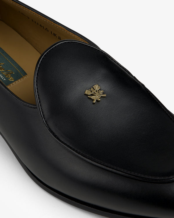 Crest Salóni Loafer: black leather loafer with a gold floral emblem on the upper, shown from an angle.