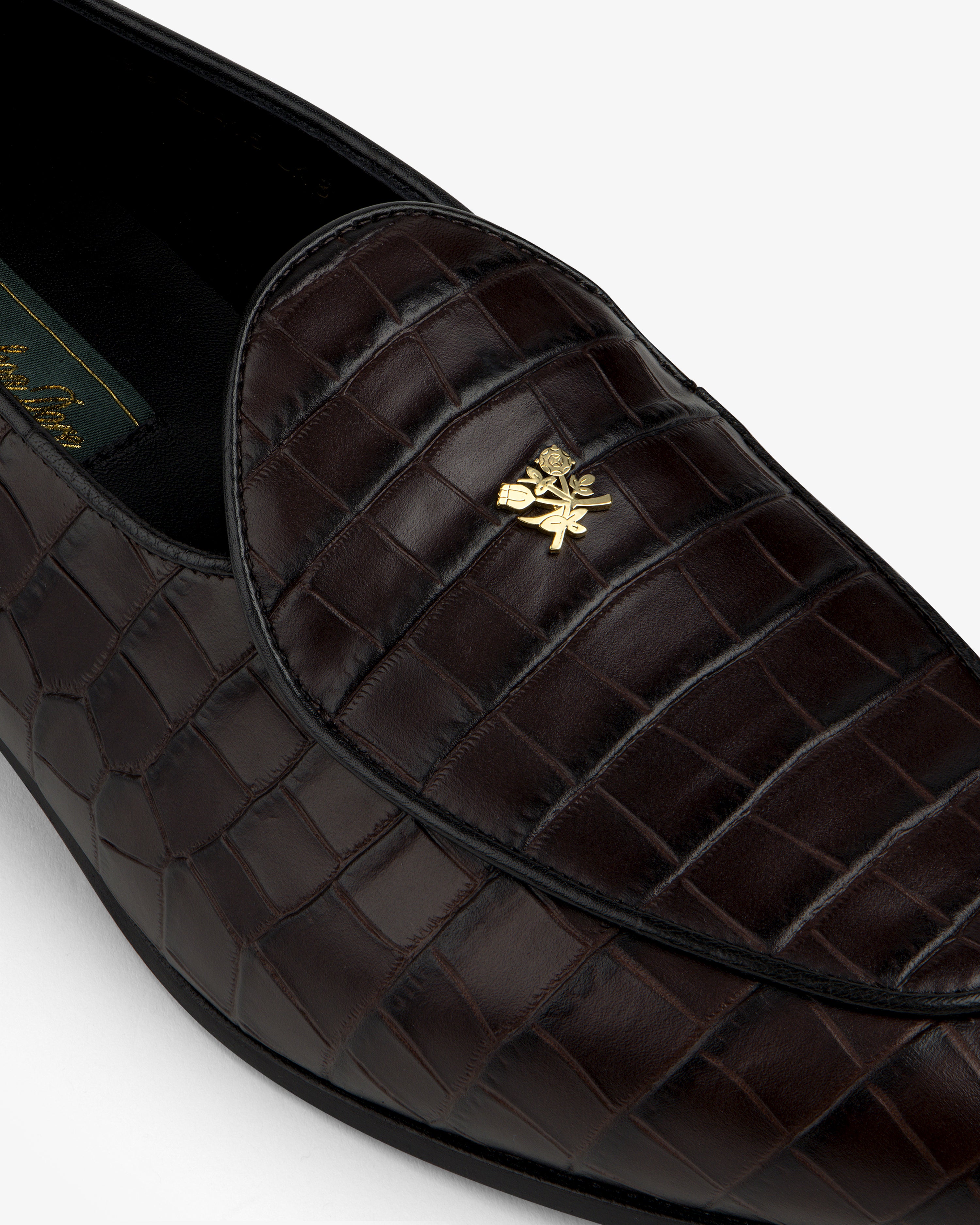 Close-up of Croc-Embossed Crest Salóni Loafer in dark brown with a gold emblem on the upper.