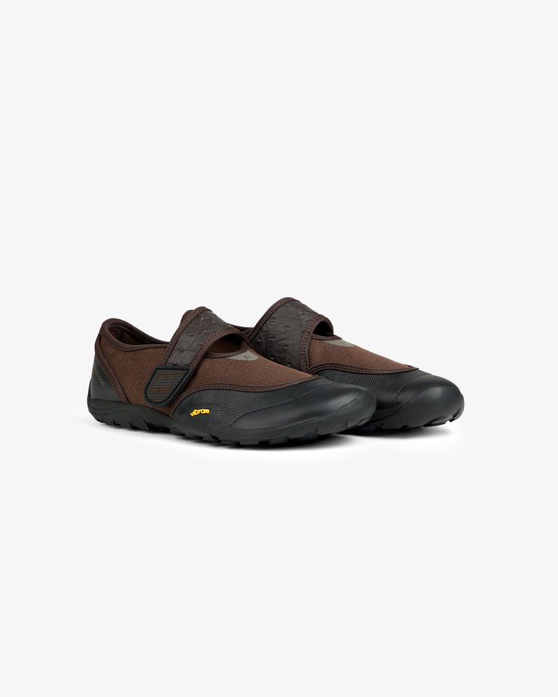 ALD / New Balance MT2 low-profile athletic shoes in brown with black toe caps, textured straps, and yellow Vibram outsoles.
