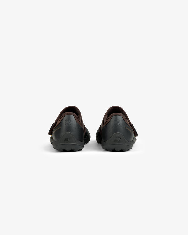 Back view of two black ALD / New Balance MT2 slip-on shoes with dark brown trim and lugged rubber outsoles.