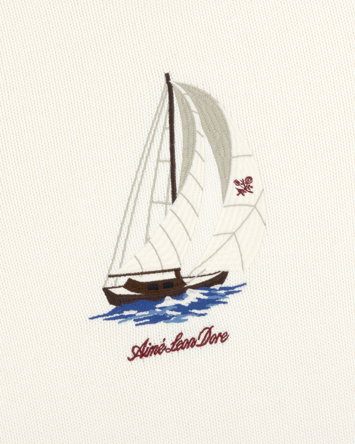 Regatta Embroidered Crewneck Sweater: Sailboat with white sails on blue water, Aimé Leon Dore text, cream fabric.