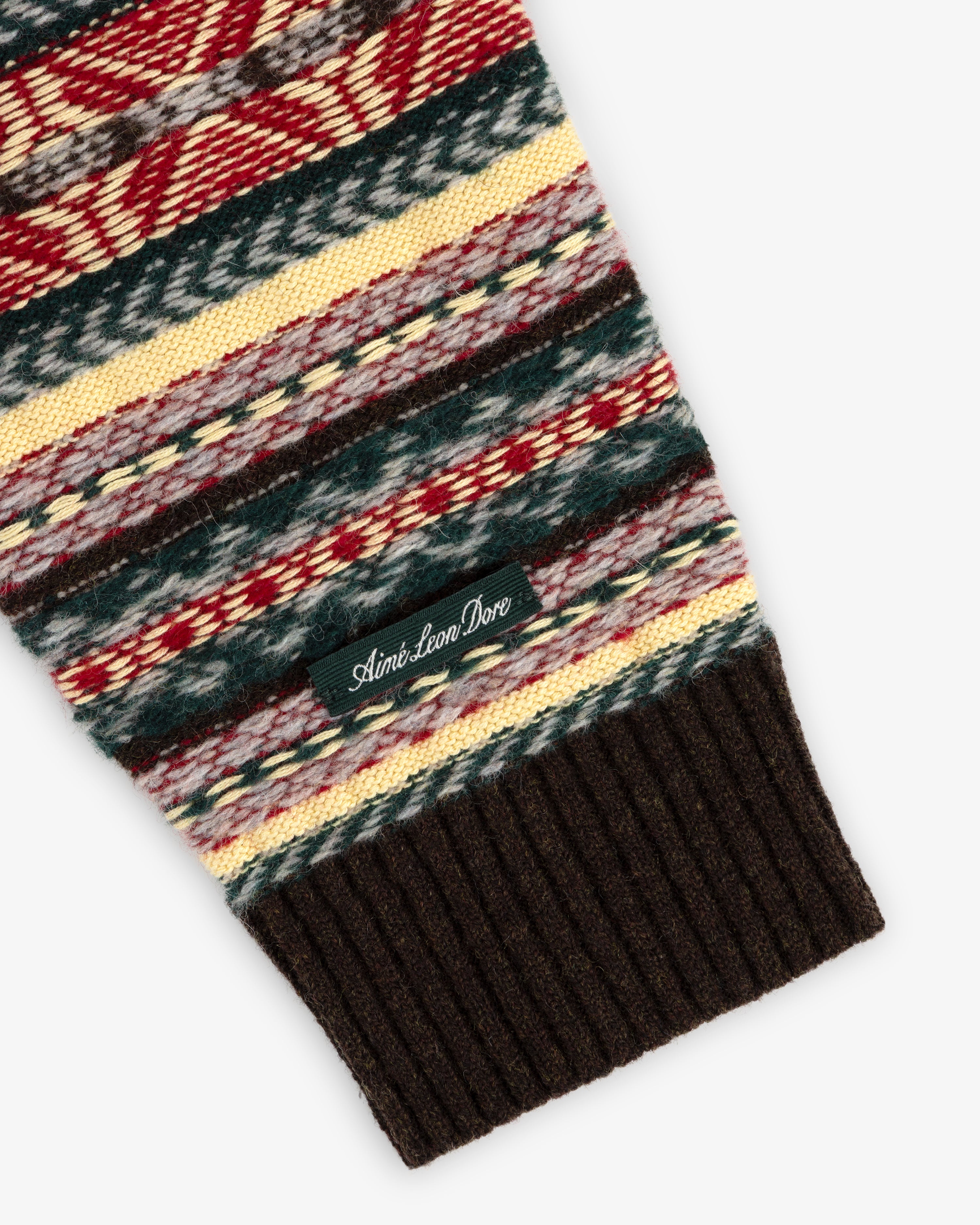 A Fair Isle V-Neck Sweater sleeve features multicolored knit, a ribbed brown cuff, and an Aimé Leon Dore label.