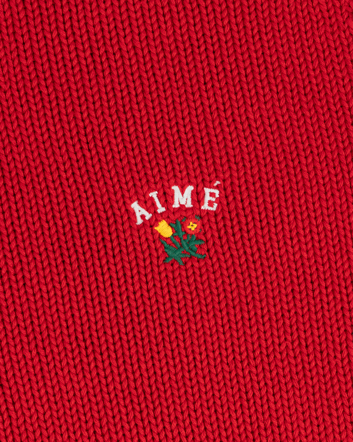 Red Crest Raglan Sweater with AIMÉ text and a small embroidered yellow flower with green leaves beneath it.
