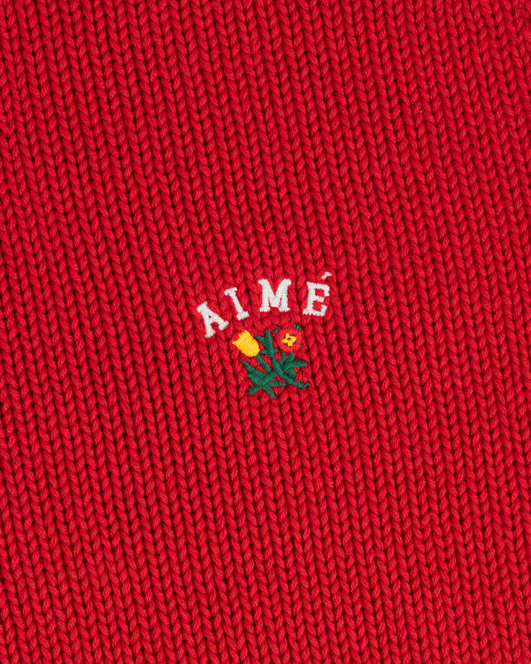 Red Crest Raglan Sweater with AIMÉ text and a small embroidered yellow flower with green leaves beneath it.