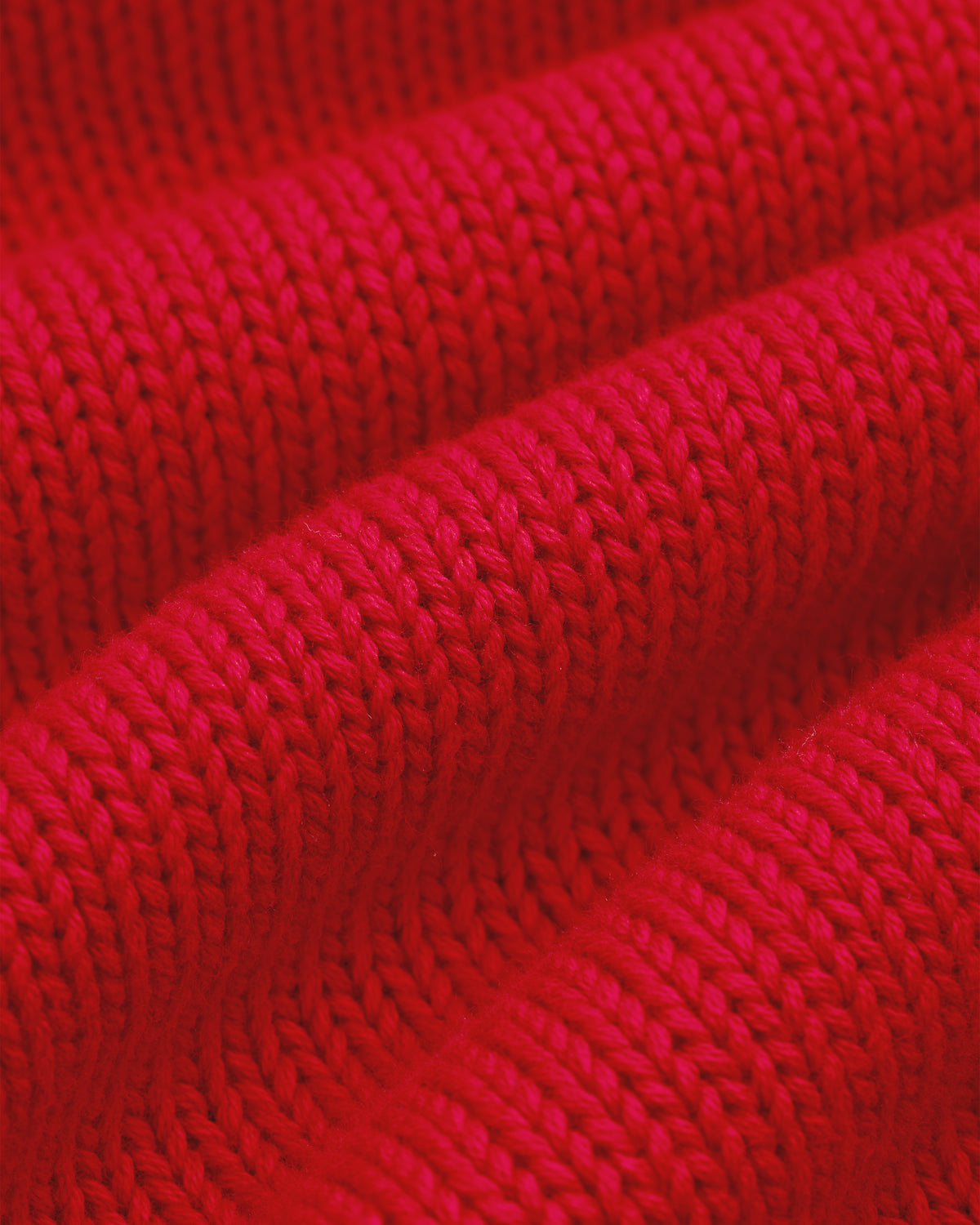 Close-up of Crest Raglan Sweater: red knit fabric with detailed, textured rows and folds.