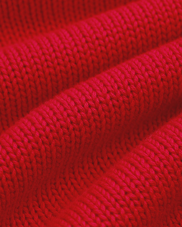 Close-up of Crest Raglan Sweater: red knit fabric with detailed, textured rows and folds.