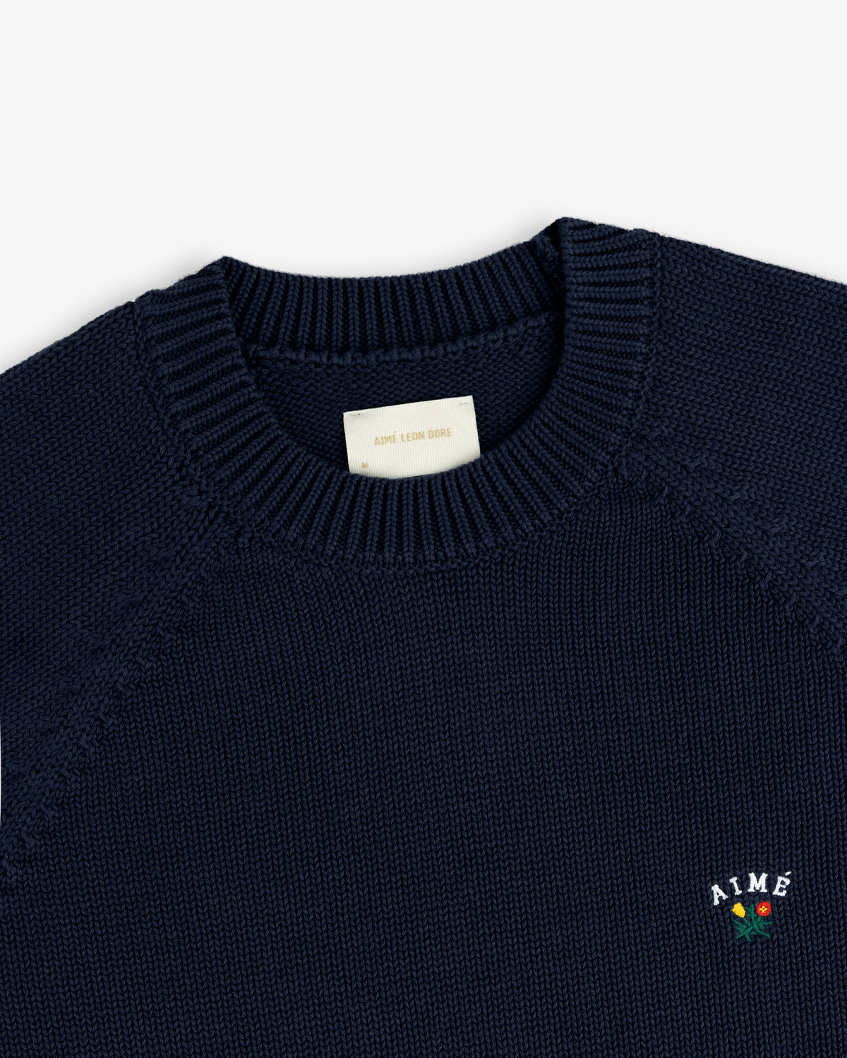 Crest Raglan Sweater: Navy crewneck knit with “AIME” and a red rose embroidered on the chest.