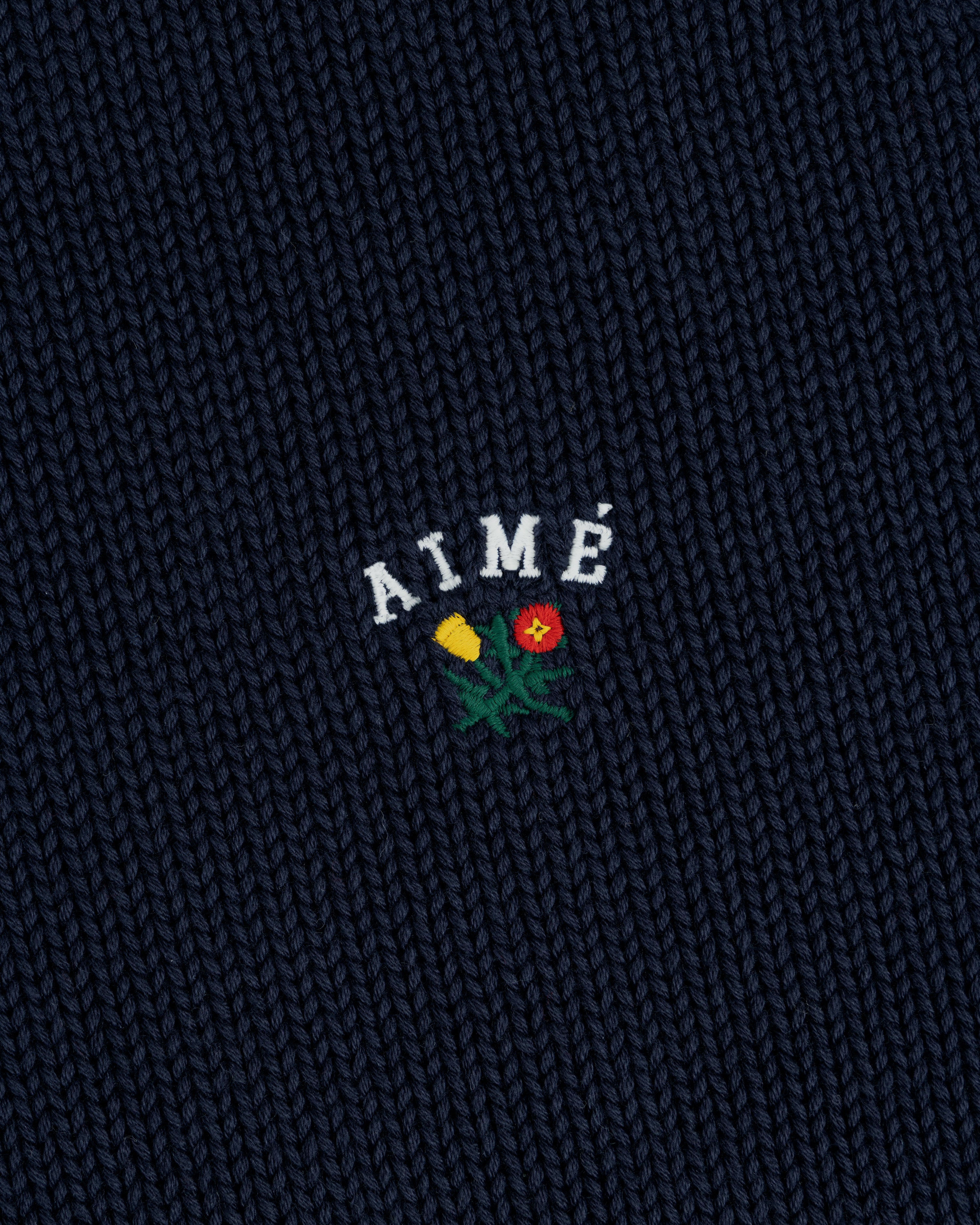 Navy Crest Raglan Sweater with AIMÉ embroidered above a yellow and red flower design.