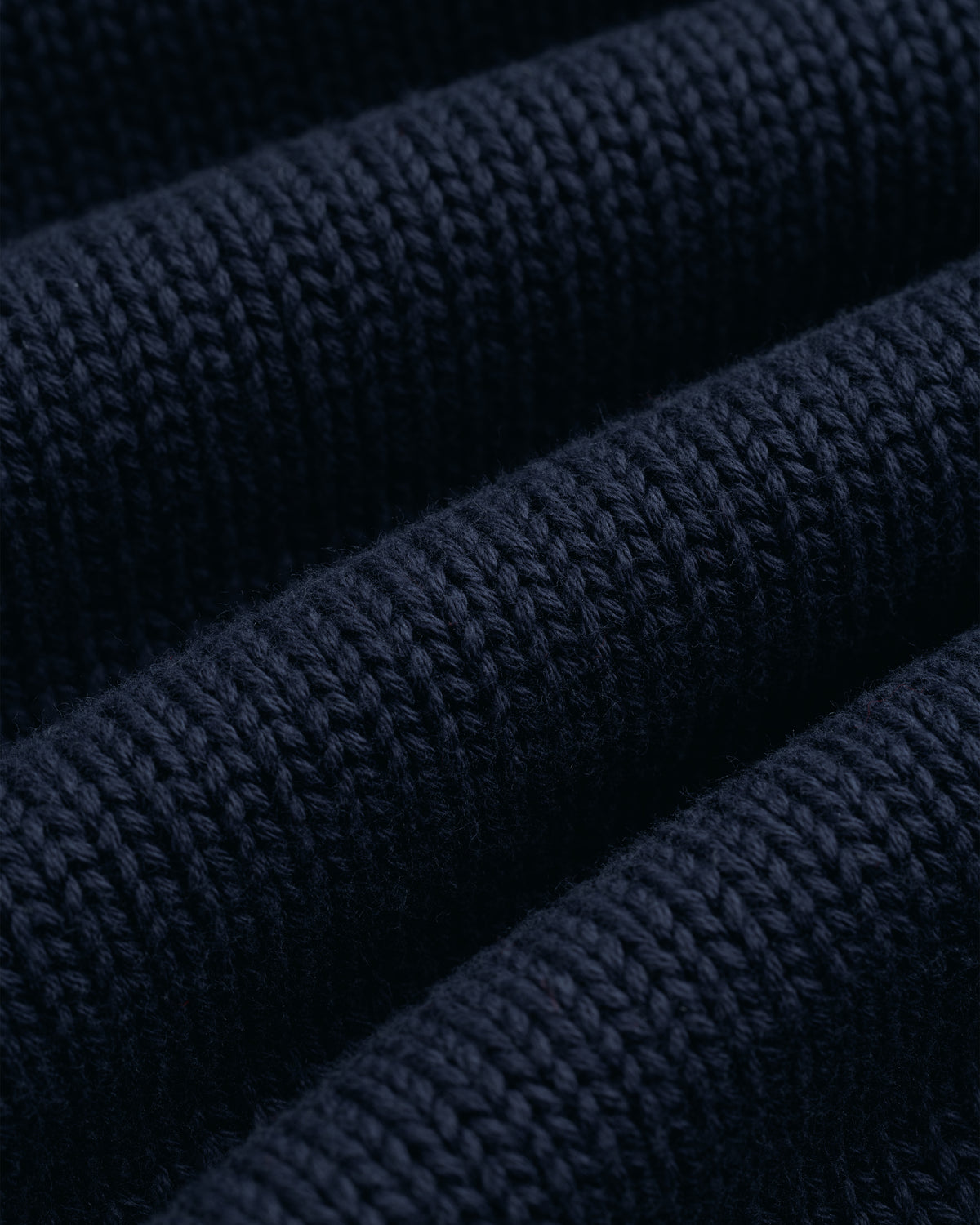 Close-up of the Crest Raglan Sweater in dark blue, showing its textured rows and visible knitted stitches.
