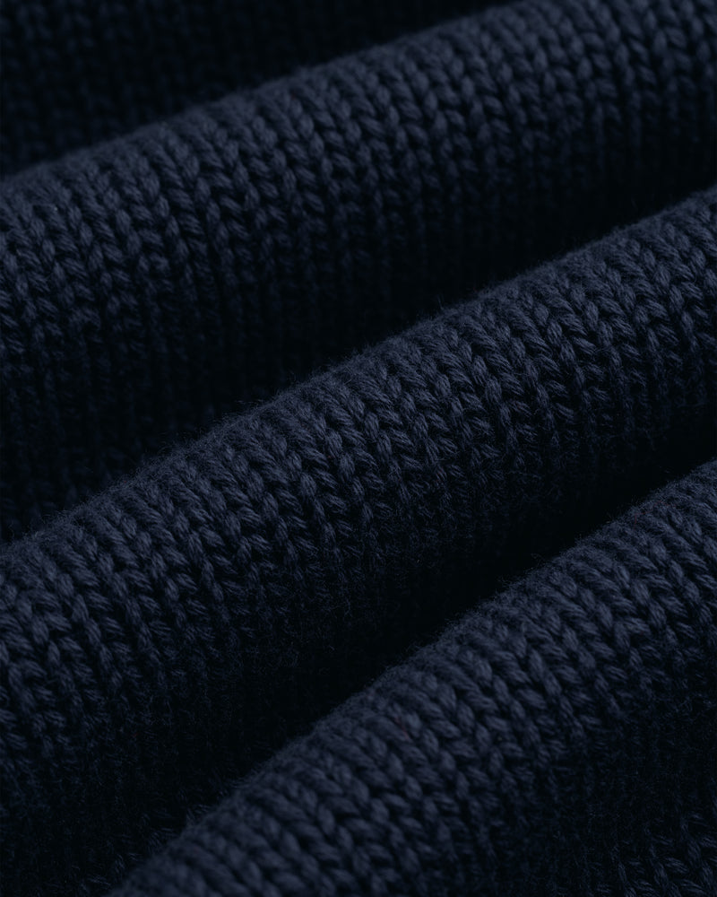 Close-up of the Crest Raglan Sweater in dark blue, showing its textured rows and visible knitted stitches.