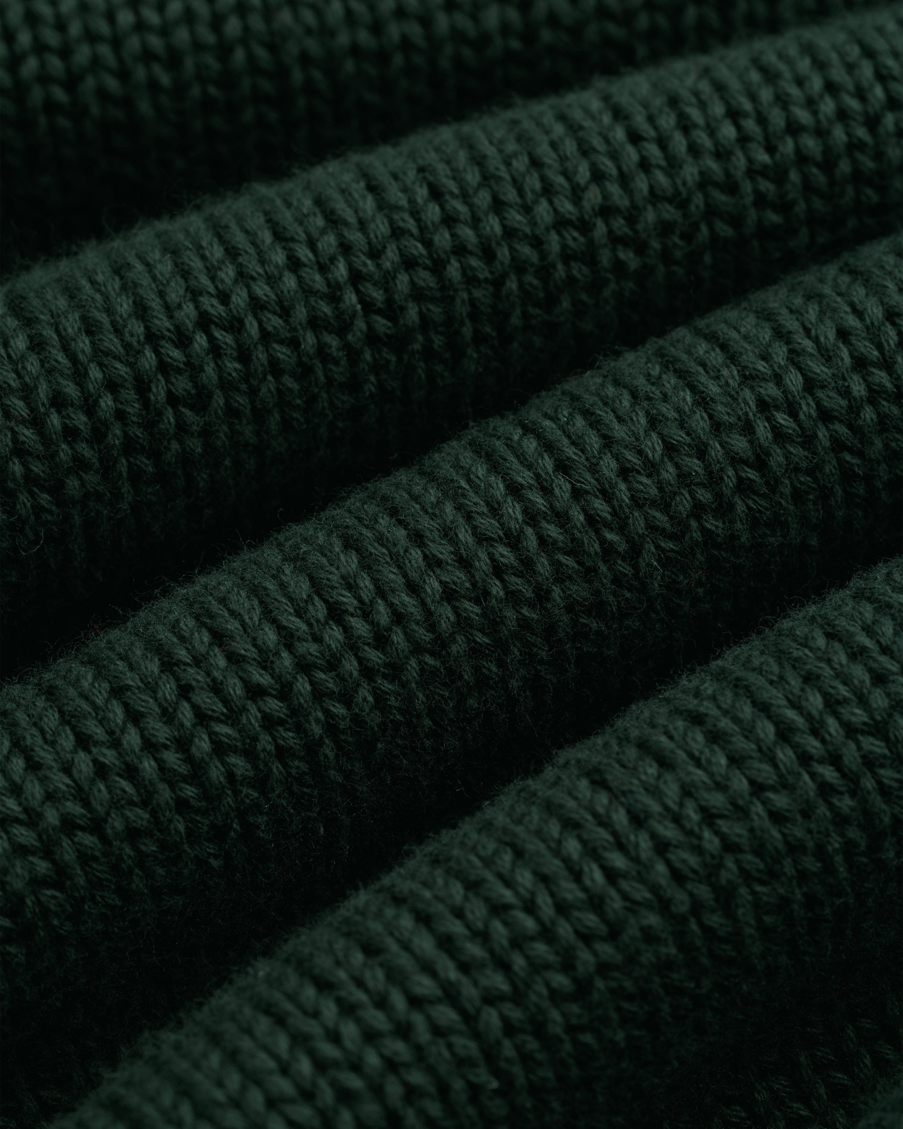 Close-up of Crest Raglan Sweater: dark green ribbed knit with textured horizontal rows and soft fibers.