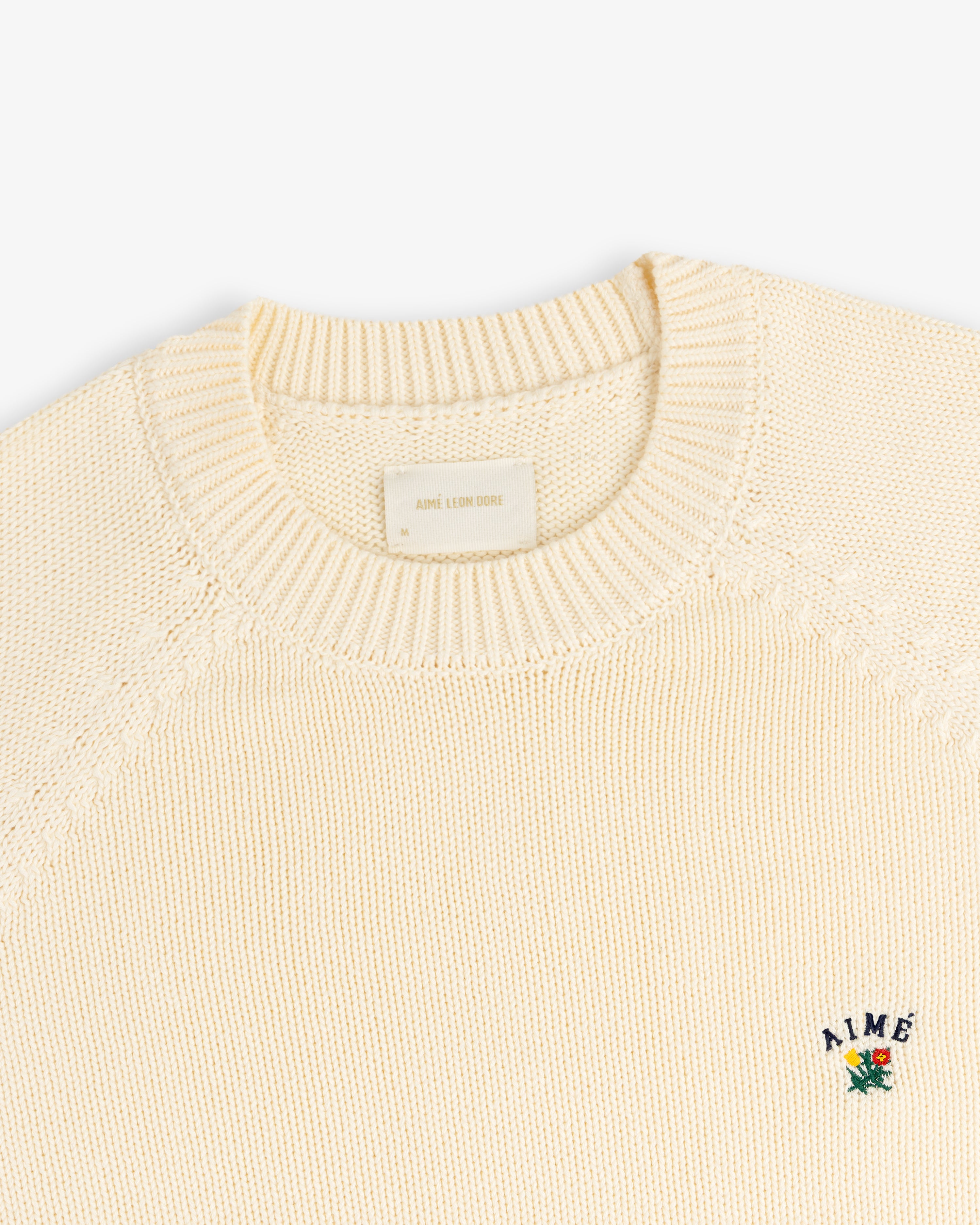Crest Raglan Sweater: Cream knit crewneck with small AIME and floral embroidery on left chest.