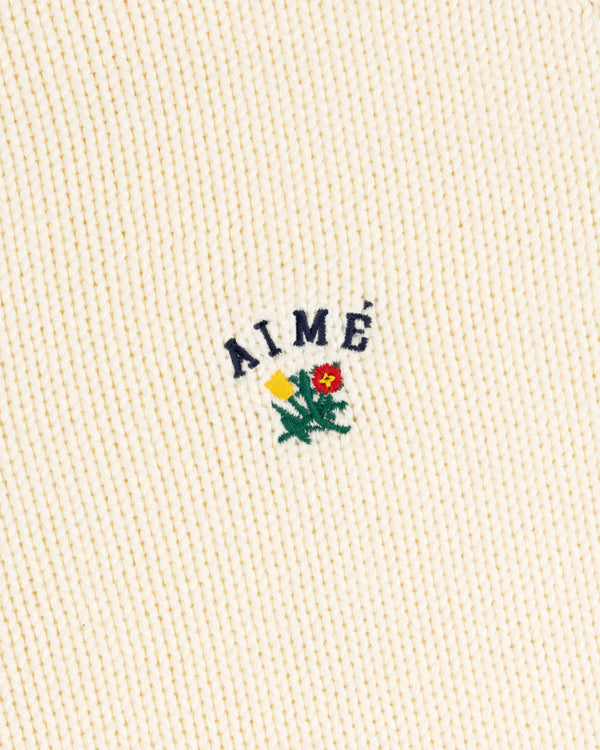 Cream ribbed Crest Raglan Sweater with AIMÉ and a yellow-red flower with green leaves embroidered above.