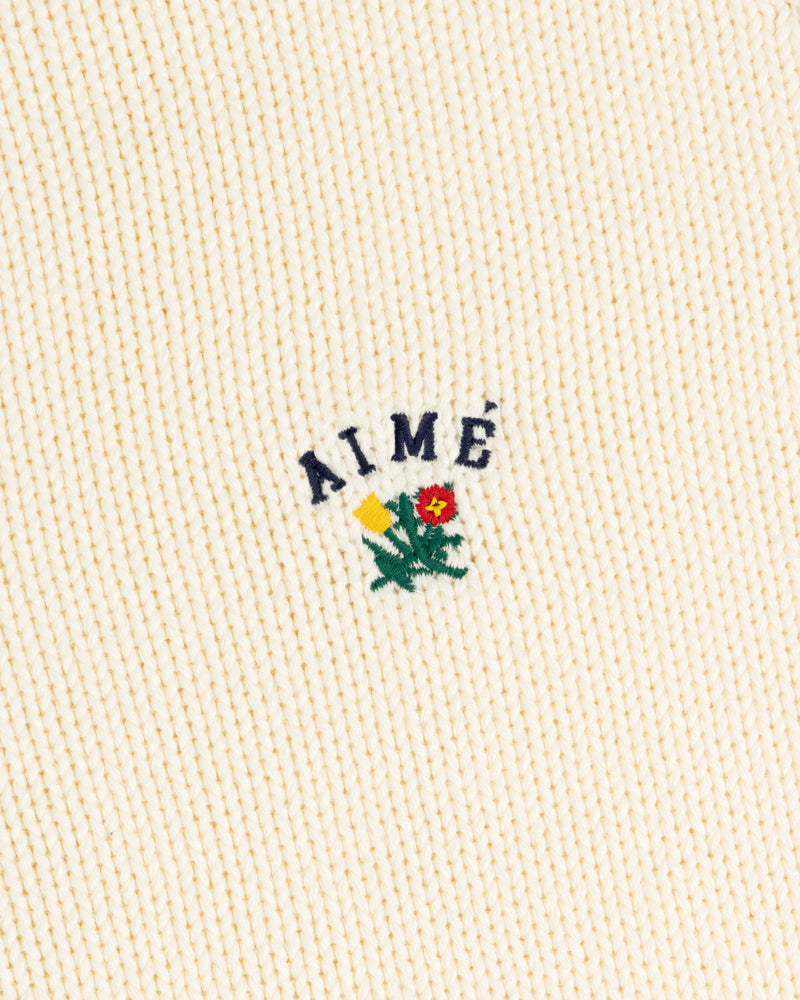 Cream ribbed Crest Raglan Sweater with AIMÉ and a yellow-red flower with green leaves embroidered above.