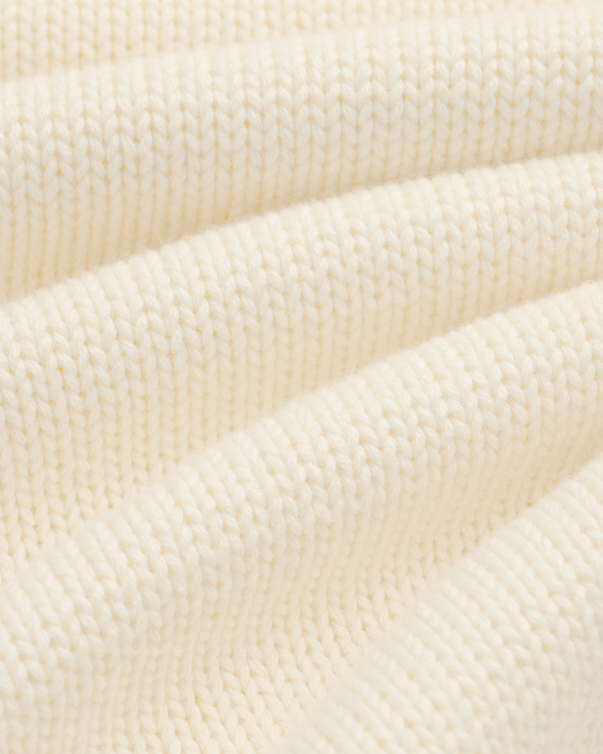 Close-up of Crest Raglan Sweater: cream ribbed knit fabric with soft, wavy folds for texture and depth.