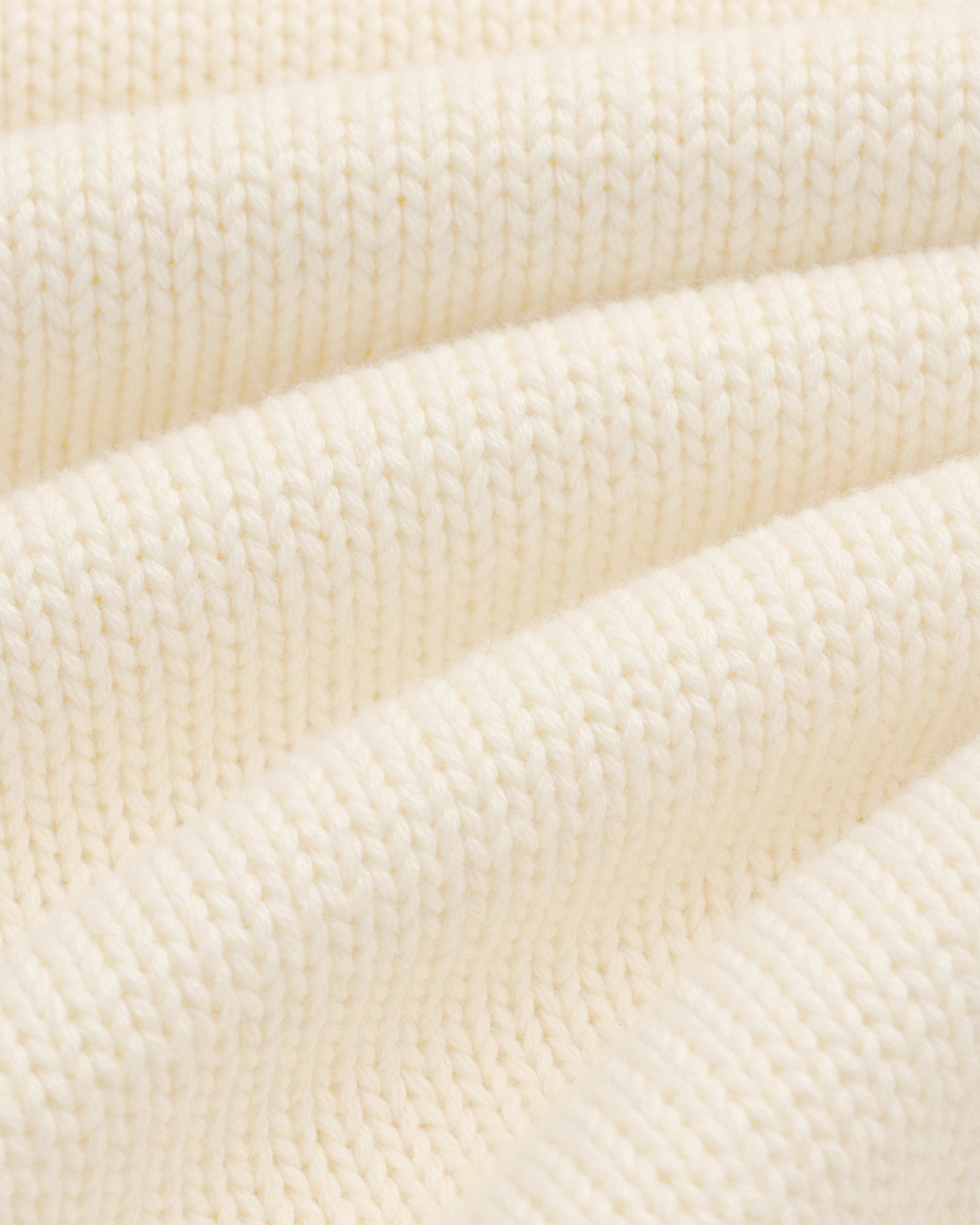 Close-up of Crest Raglan Sweater: cream ribbed knit fabric with soft, wavy folds for texture and depth.