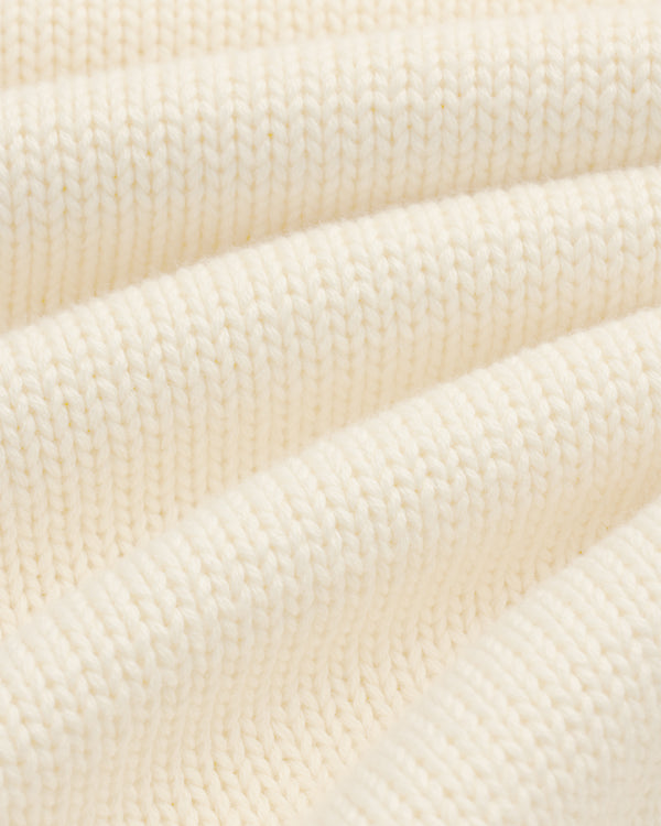 Close-up of Crest Raglan Sweater: cream ribbed knit fabric with soft, wavy folds for texture and depth.