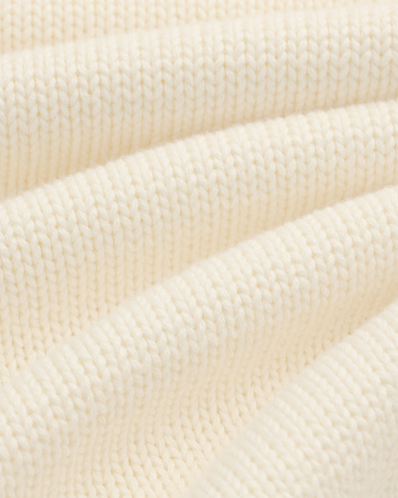 Close-up of Crest Raglan Sweater: cream ribbed knit fabric with soft, wavy folds for texture and depth.
