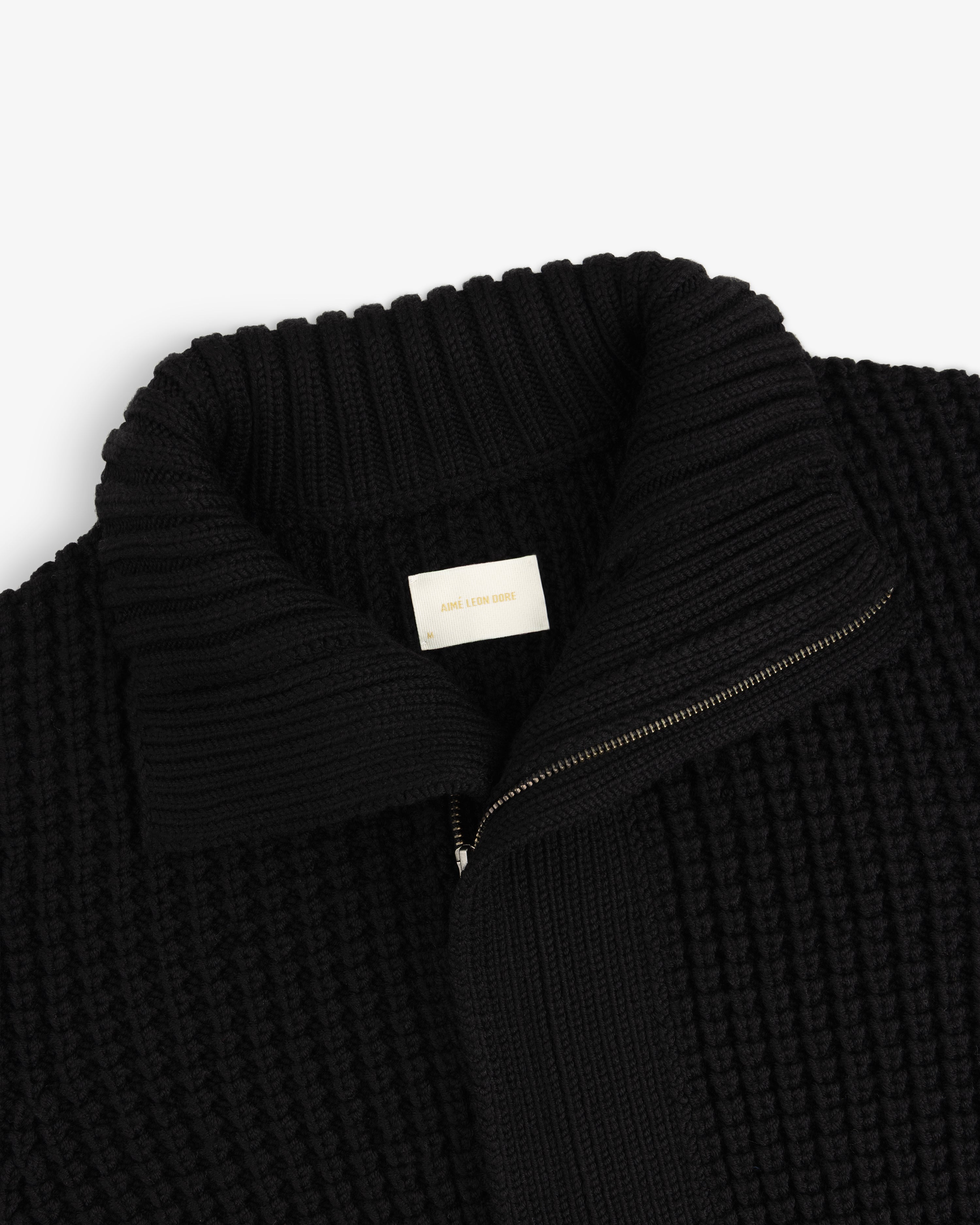 Black ribbed knit Merino Wool Full Zip Sweater with a high collar and an interior brand label.