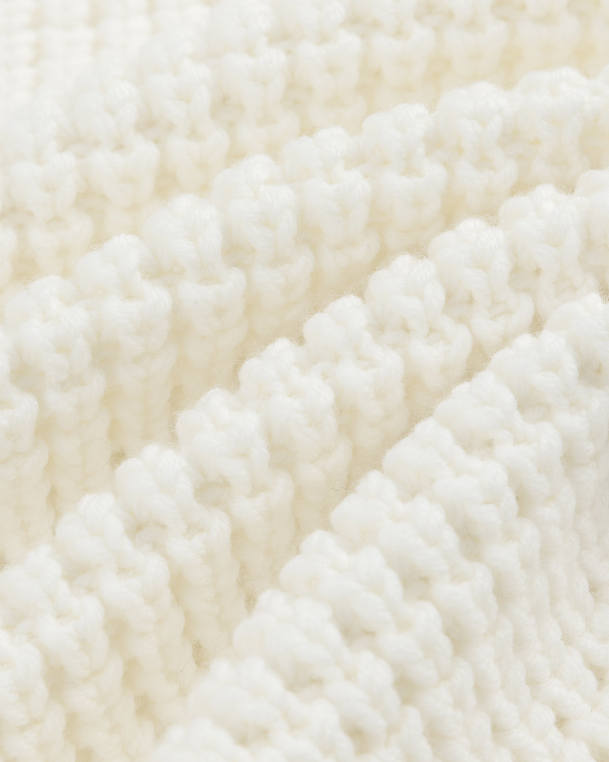 Close-up of a white Merino Wool Full Zip Sweater showing ribbed knit fabric with soft, vertical folds.