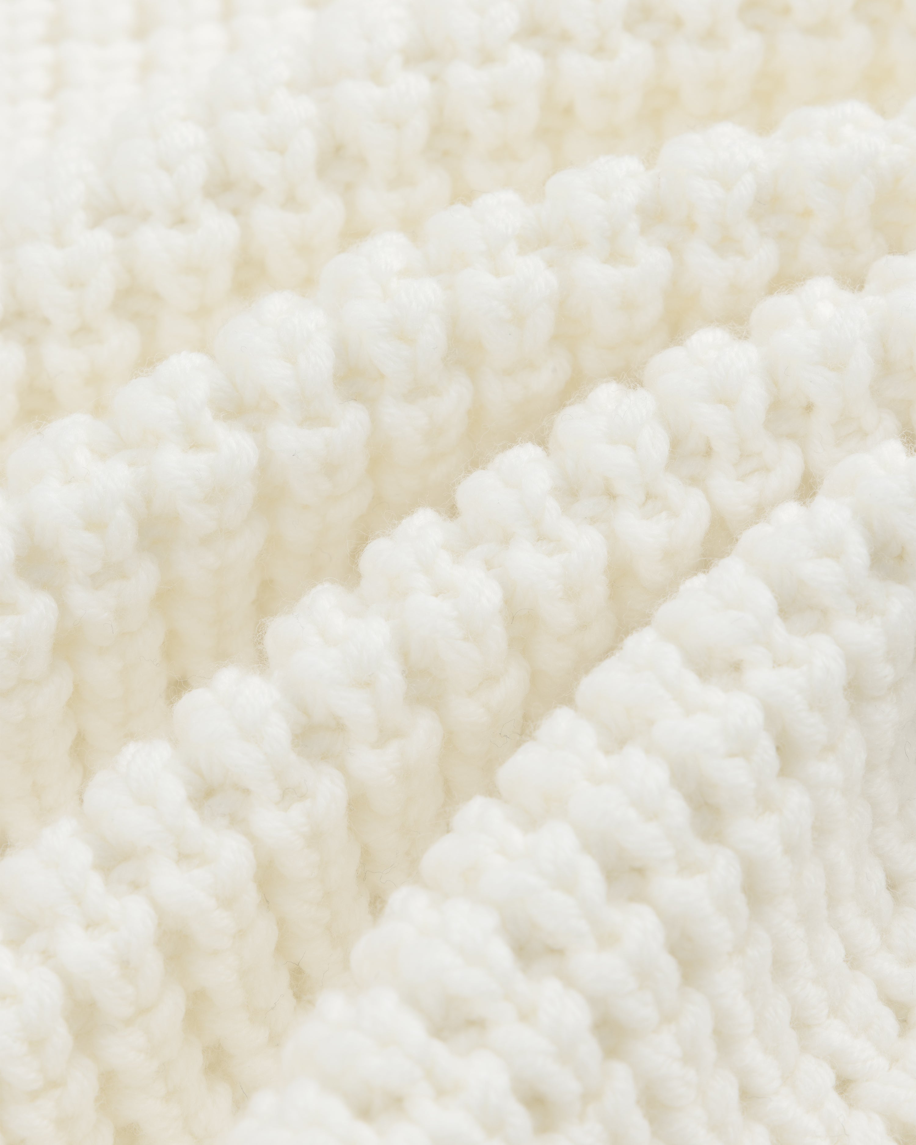 Close-up of a white Merino Wool Full Zip Sweater showing ribbed knit fabric with soft, vertical folds.