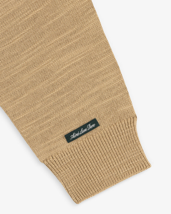 Slub Merino Wool Sweater sleeve in tan knit with a ribbed cuff and a small branded tag.