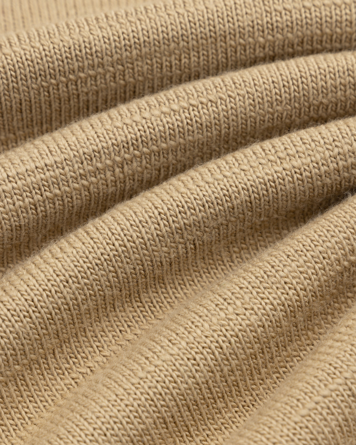 Close-up of tan Slub Merino Wool Sweater knit fabric with textured diagonal folds.
