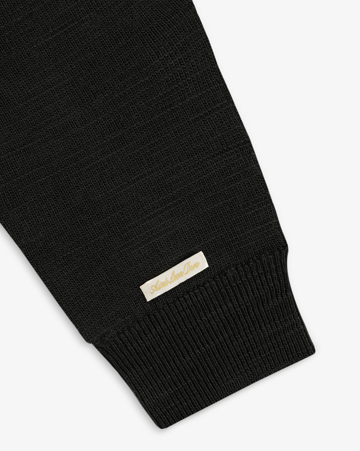 Black Slub Merino Wool Sweater sleeve with a ribbed cuff and a small, rectangular logo tag near the wrist.