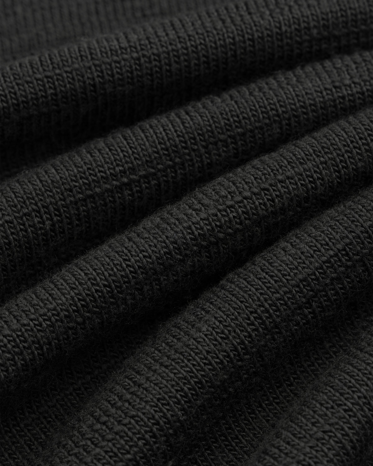 Close-up of black Slub Merino Wool Sweater knit fabric with visible texture and folds.