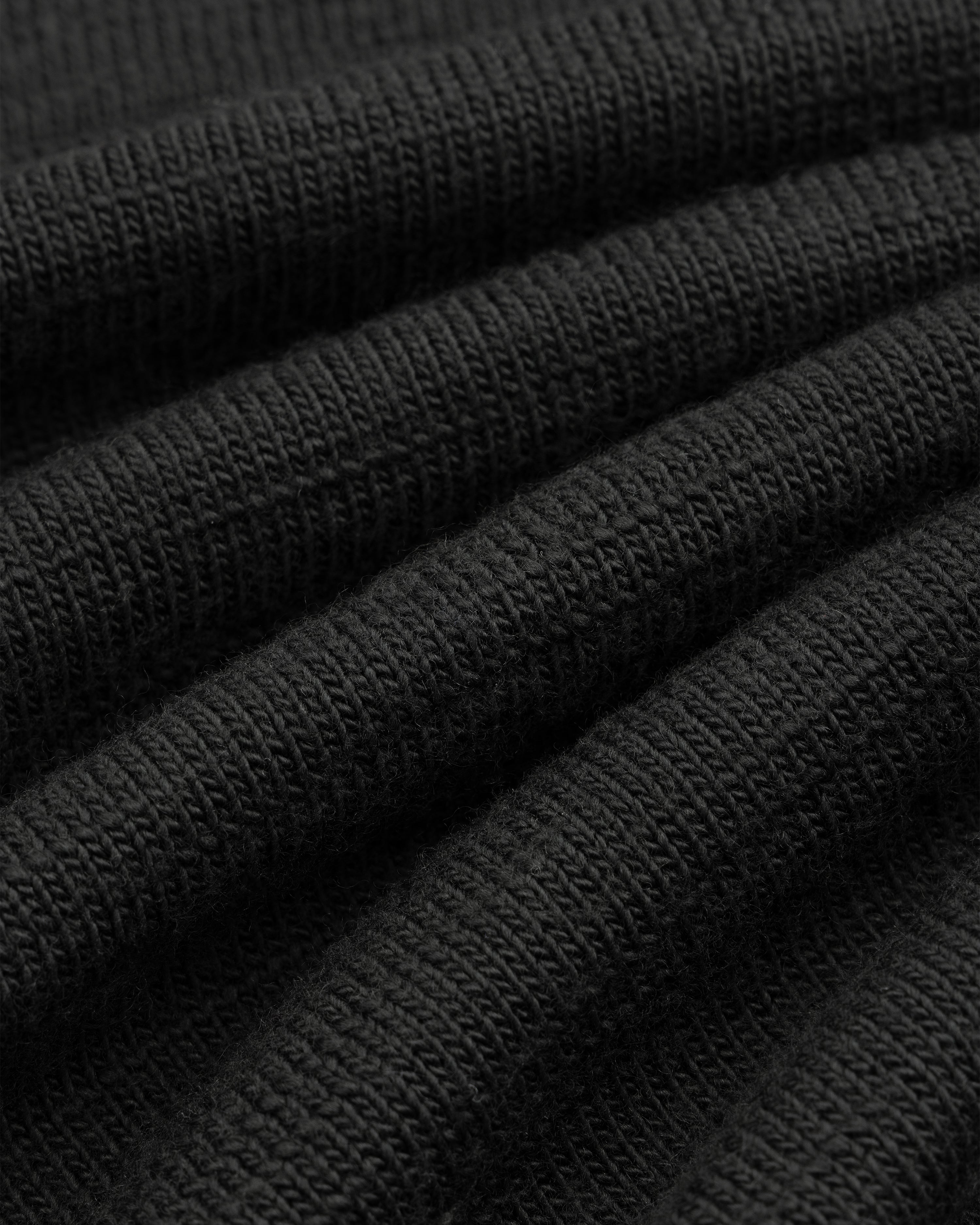 Close-up of black Slub Merino Wool Sweater knit fabric with visible texture and folds.