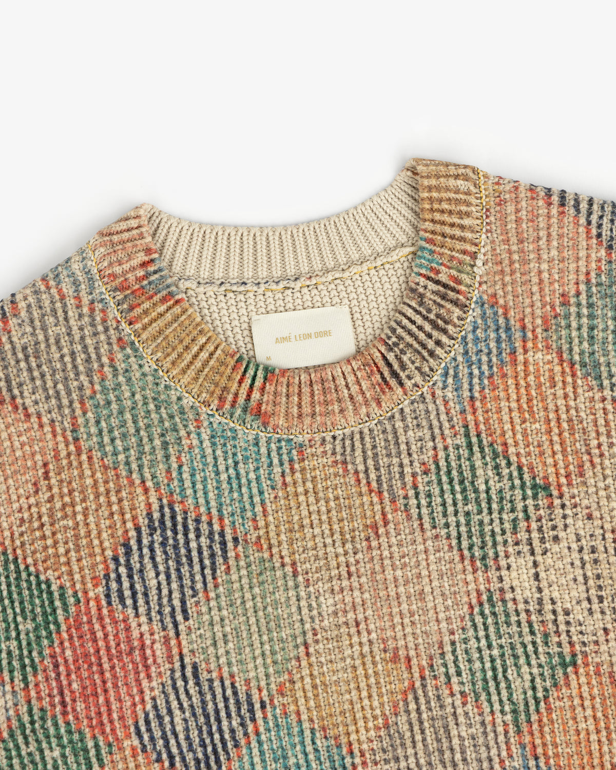 Close-up of the Kilim Argyle Crewneck Sweater, featuring a multicolored argyle pattern and beige collar.