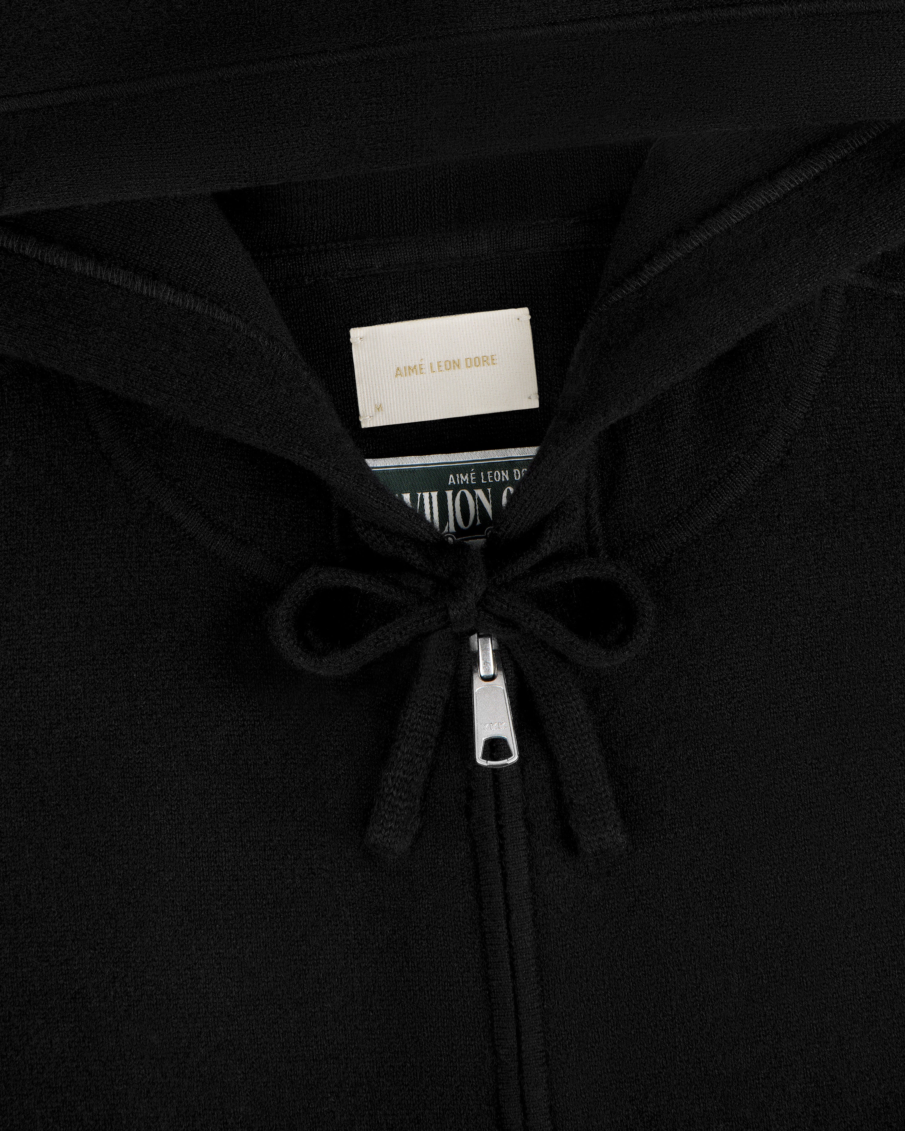 Close-up of the Full-Zip Pavilion Cashmere Hoodie in black, featuring drawstrings and an Aimé Leon Dore label in the collar.