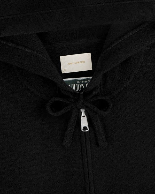 Close-up of the Full-Zip Pavilion Cashmere Hoodie in black, featuring drawstrings and an Aimé Leon Dore label in the collar.