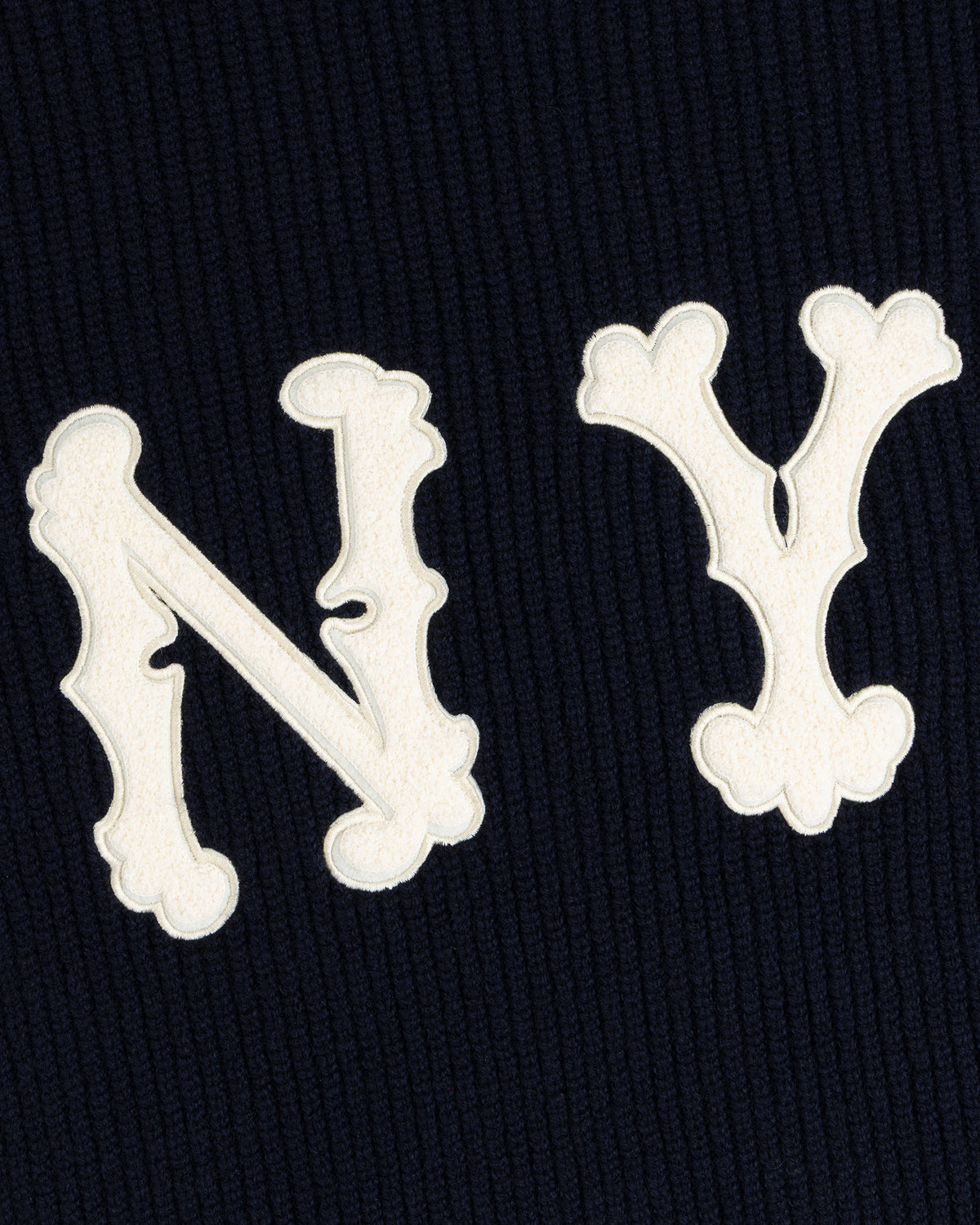 White ‘N’ and ‘Y’ letters featured on the NY Highlanders Ribbed Wool Crewneck Sweater’s dark, ribbed background.