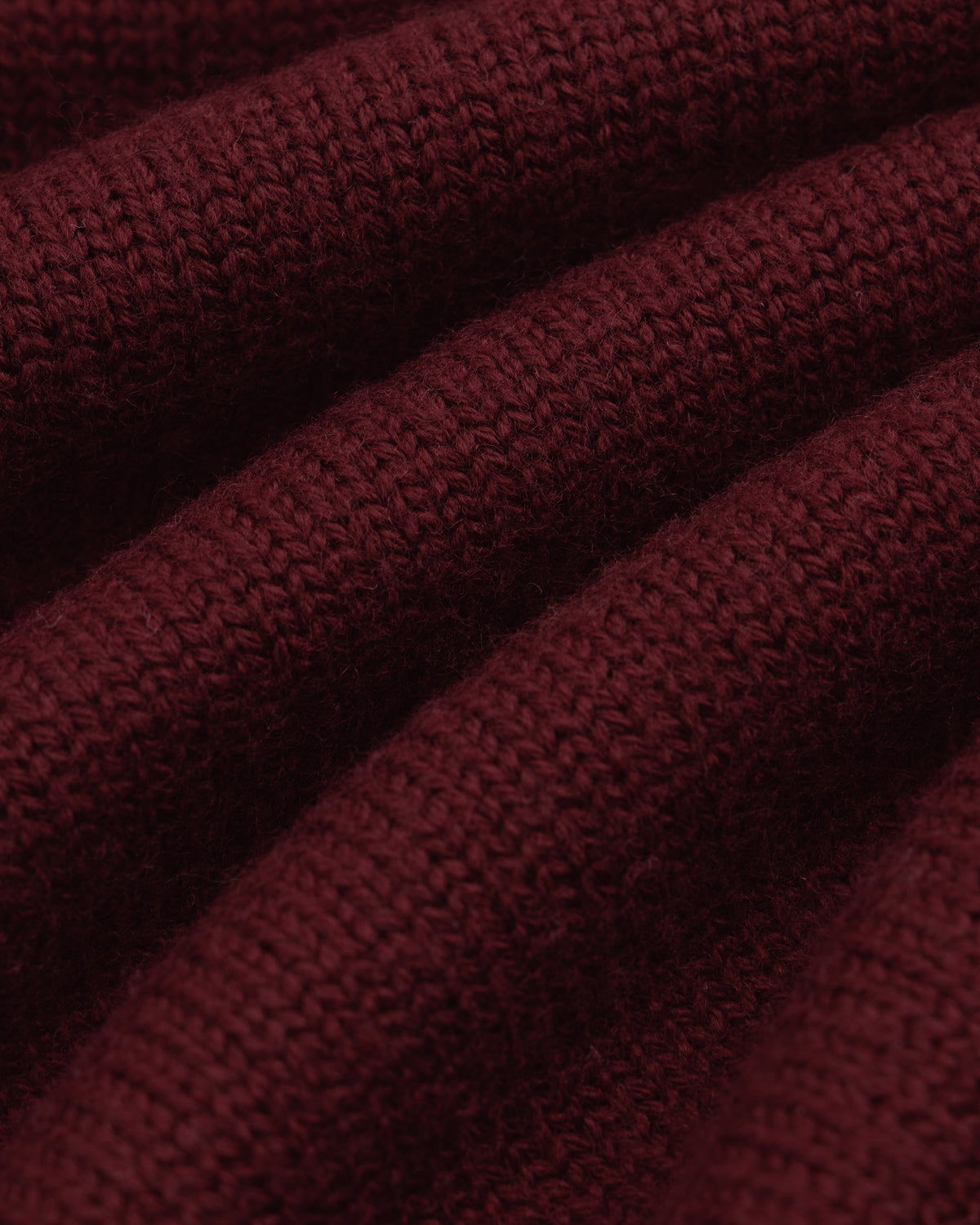 Close-up of deep red Long-Sleeve Merino Polo knit fabric with diagonal folds.