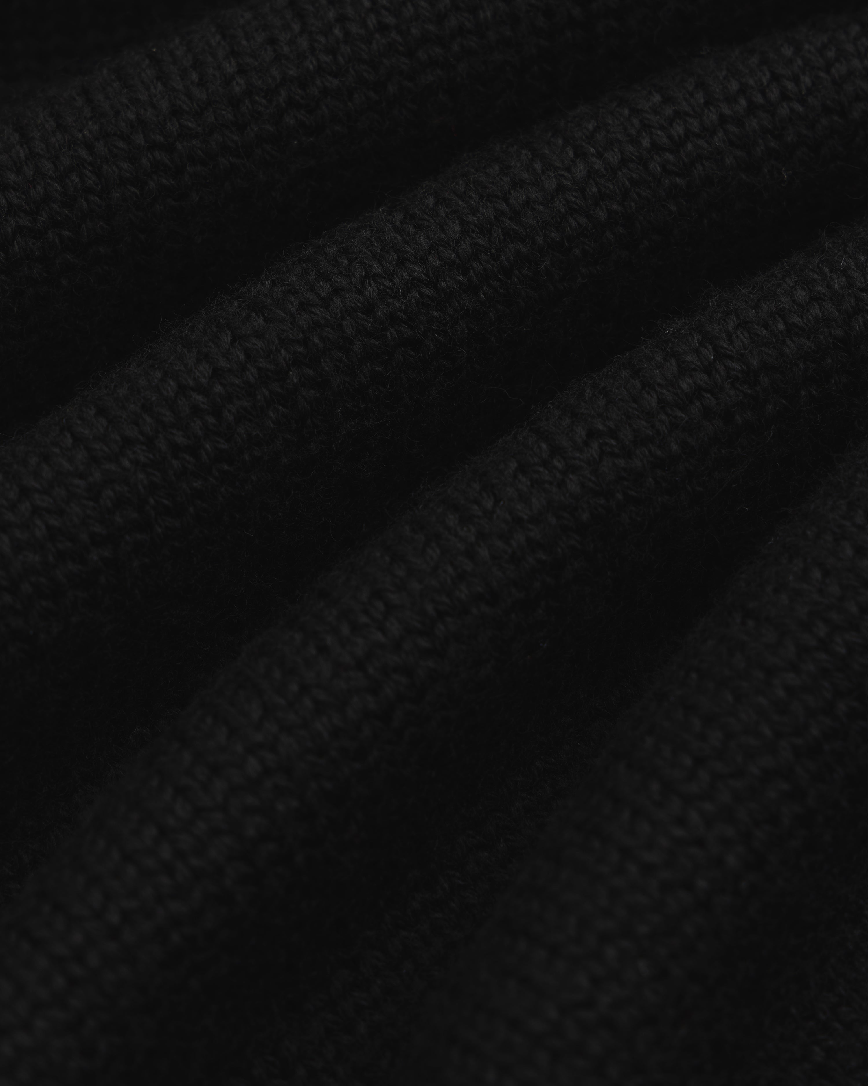Close-up of black knit fabric from a Long-Sleeve Merino Polo with diagonal folds.